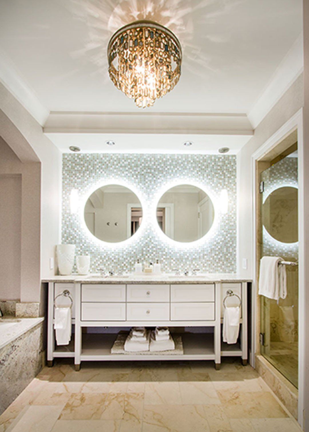 Elegant white bathroom with double vanity, round lighted mirrors, and patterned wall.