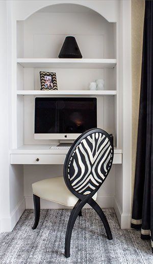 Built-in white desk with a zebra-print chair, computer, and shelving with decor.