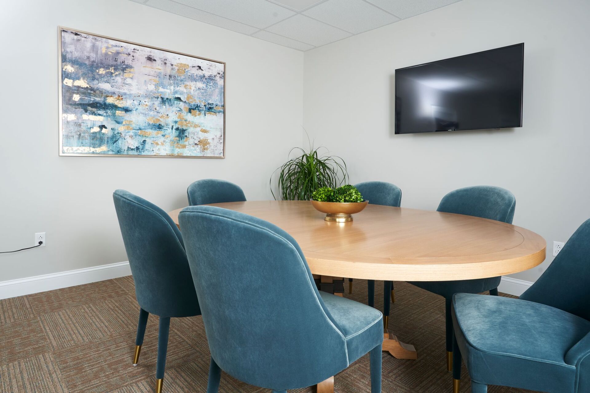 A modern meeting room with a round wooden table, teal chairs, and abstract art.