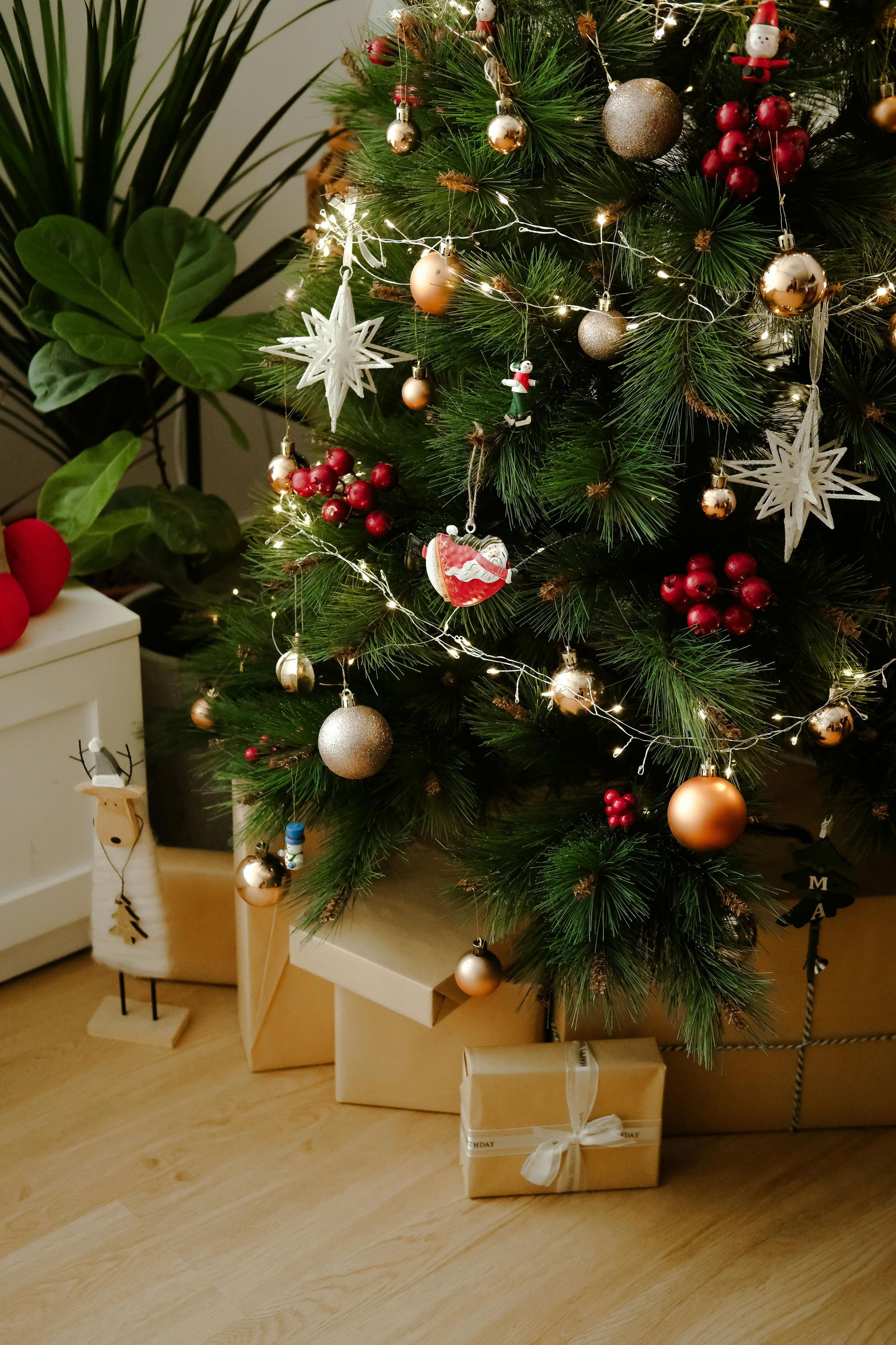 Decorated Christmas tree with ornaments and lights, surrounded by gifts and a houseplant.