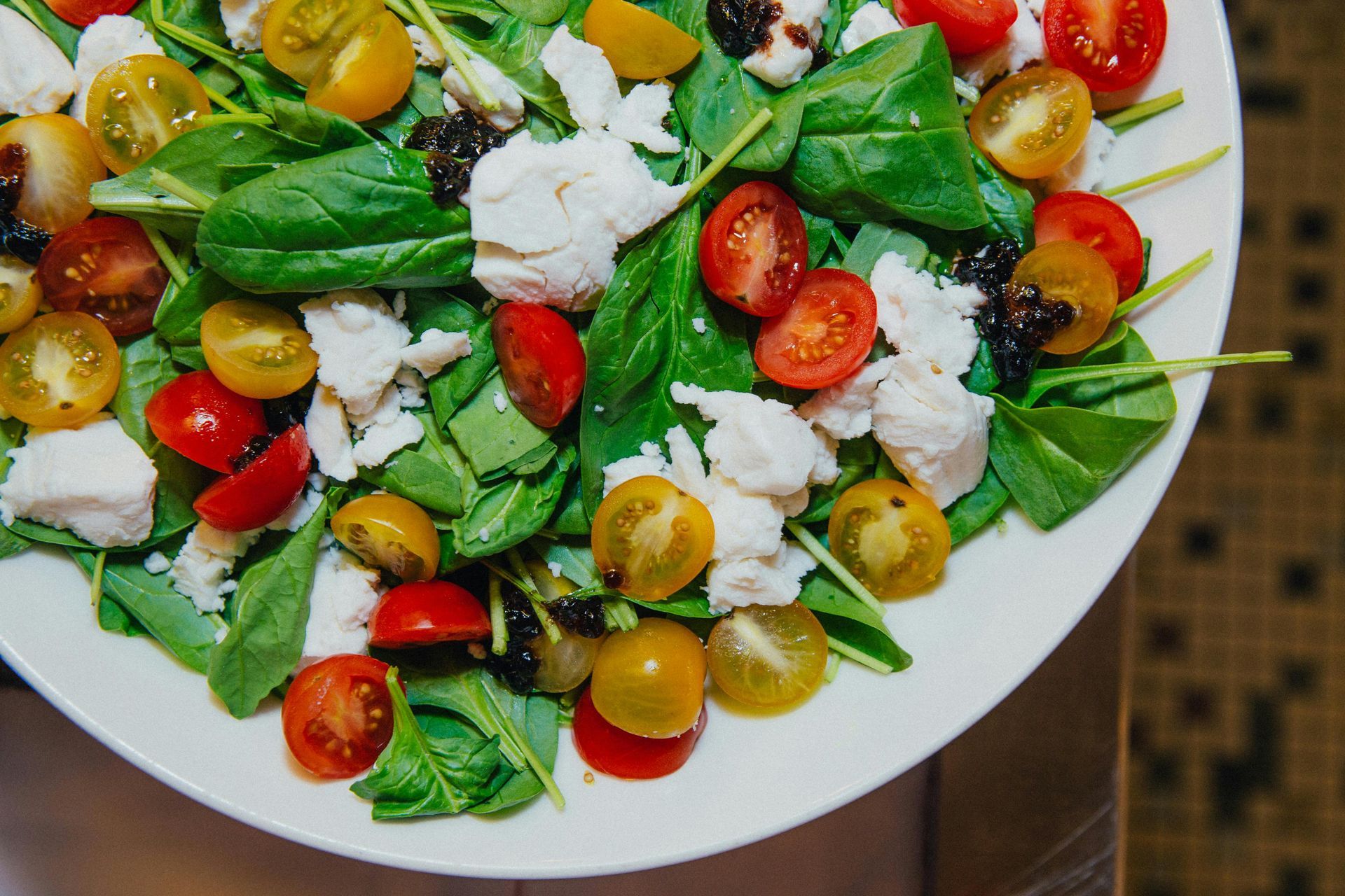 Salad with spinach, cherry tomatoes (yellow and red), and white cheese on a white plate.