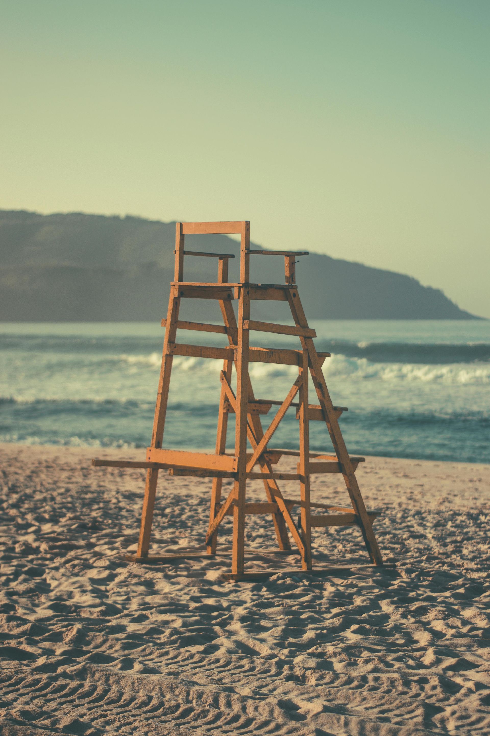 Wooden lifeguard stand on a sandy beach, ocean waves in the background, under a clear sky.