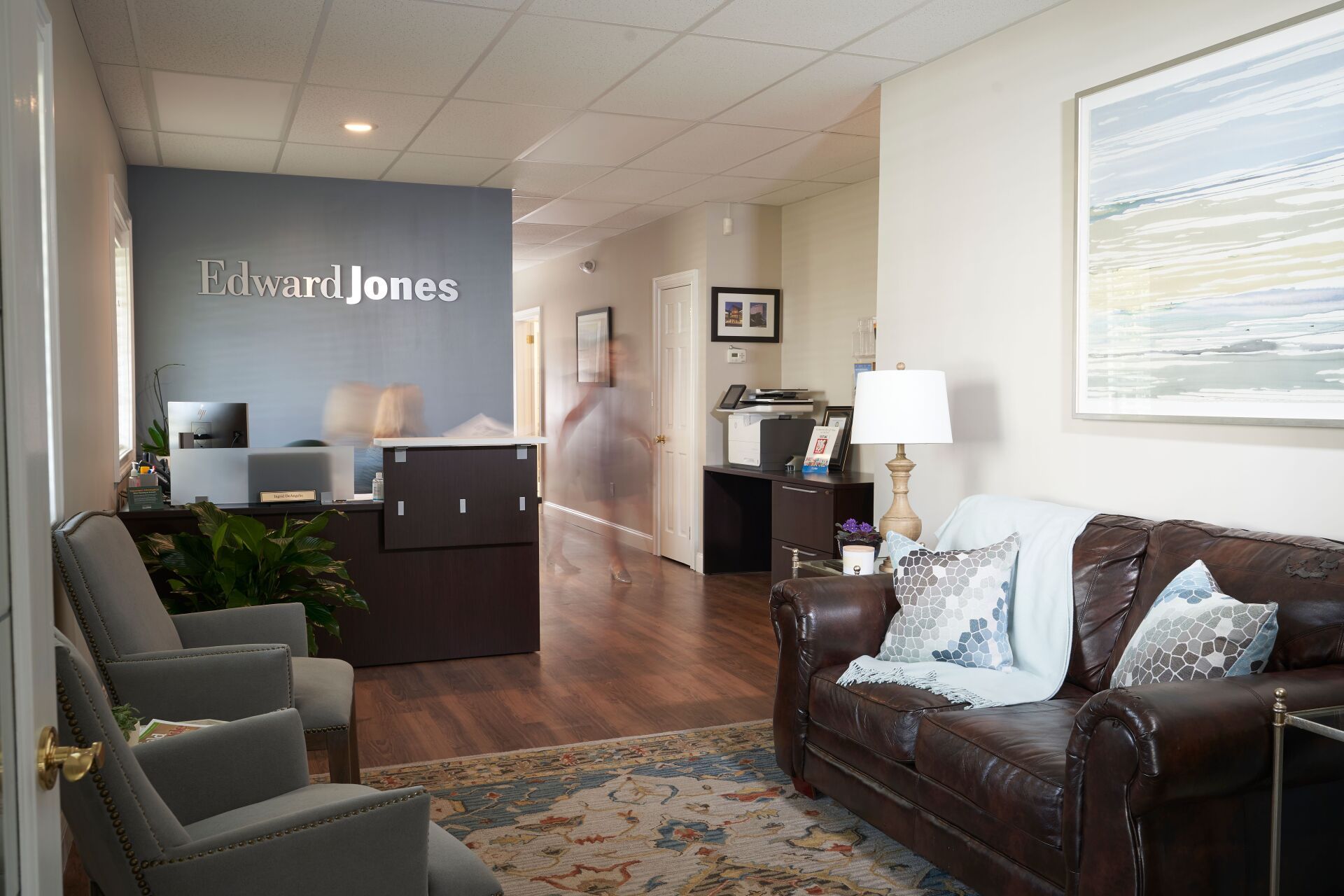 Office reception area with dark wood floors, blue accent wall, and leather sofa.