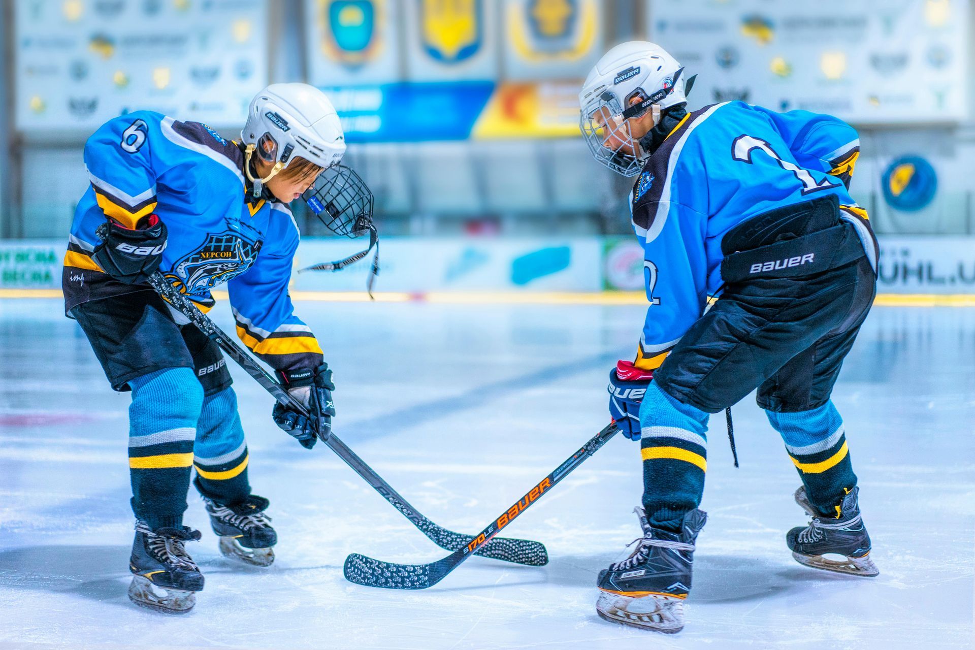 Two hockey players face off on ice, wearing blue jerseys and helmets.