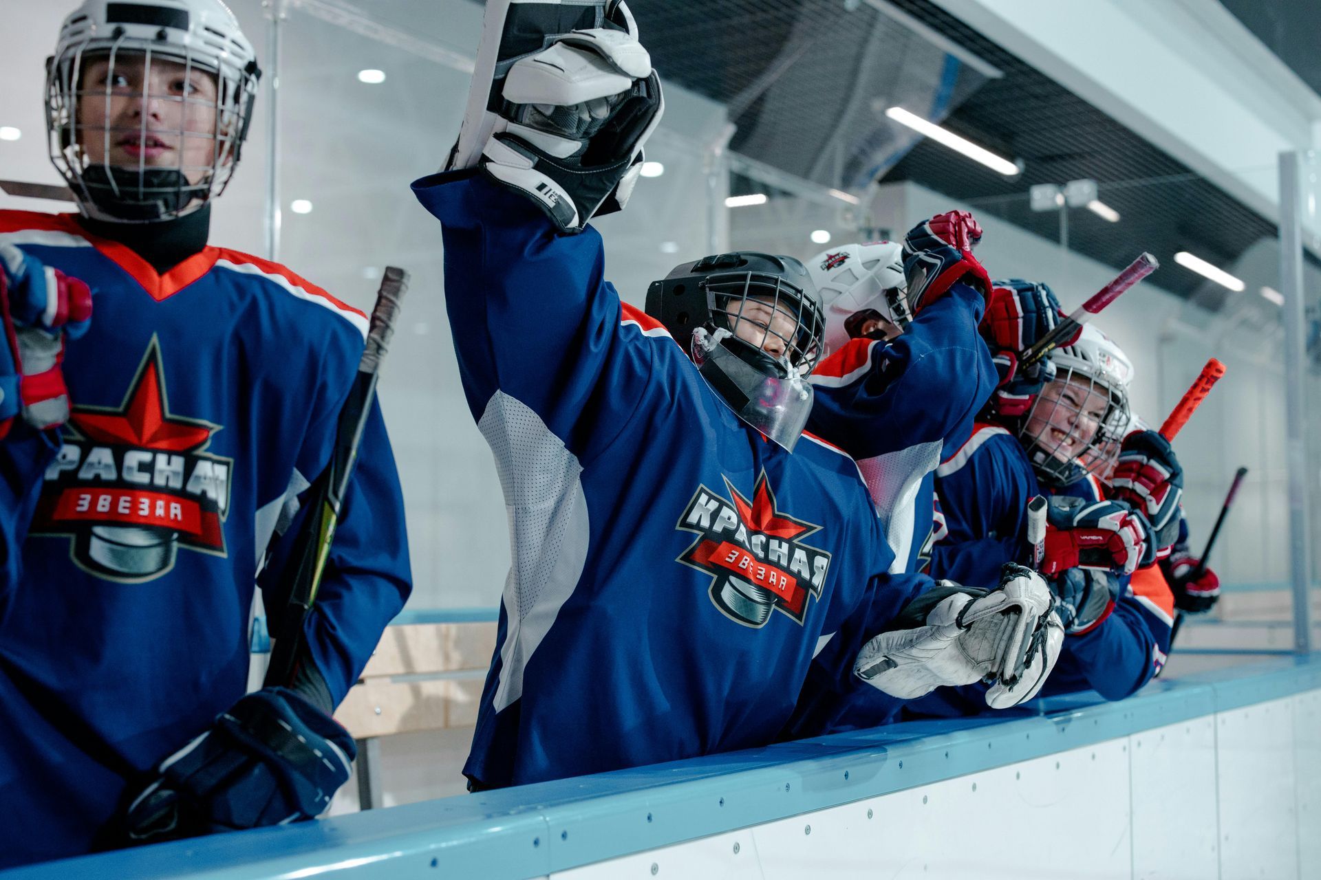 Hockey players in blue jerseys celebrating on the bench, raising gloved hands in a rink.