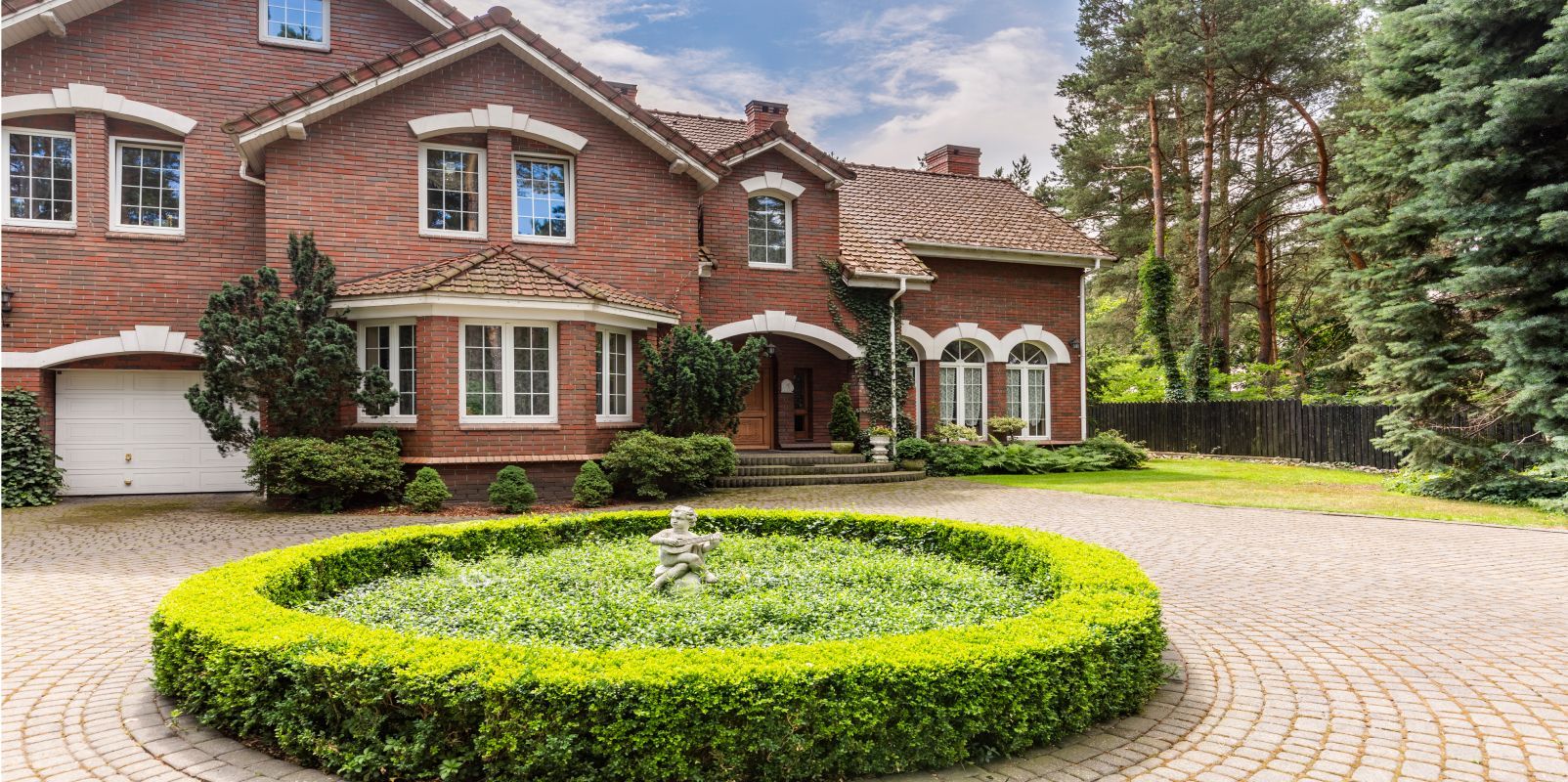 A large brick house with a circular driveway and a fountain in front of it.