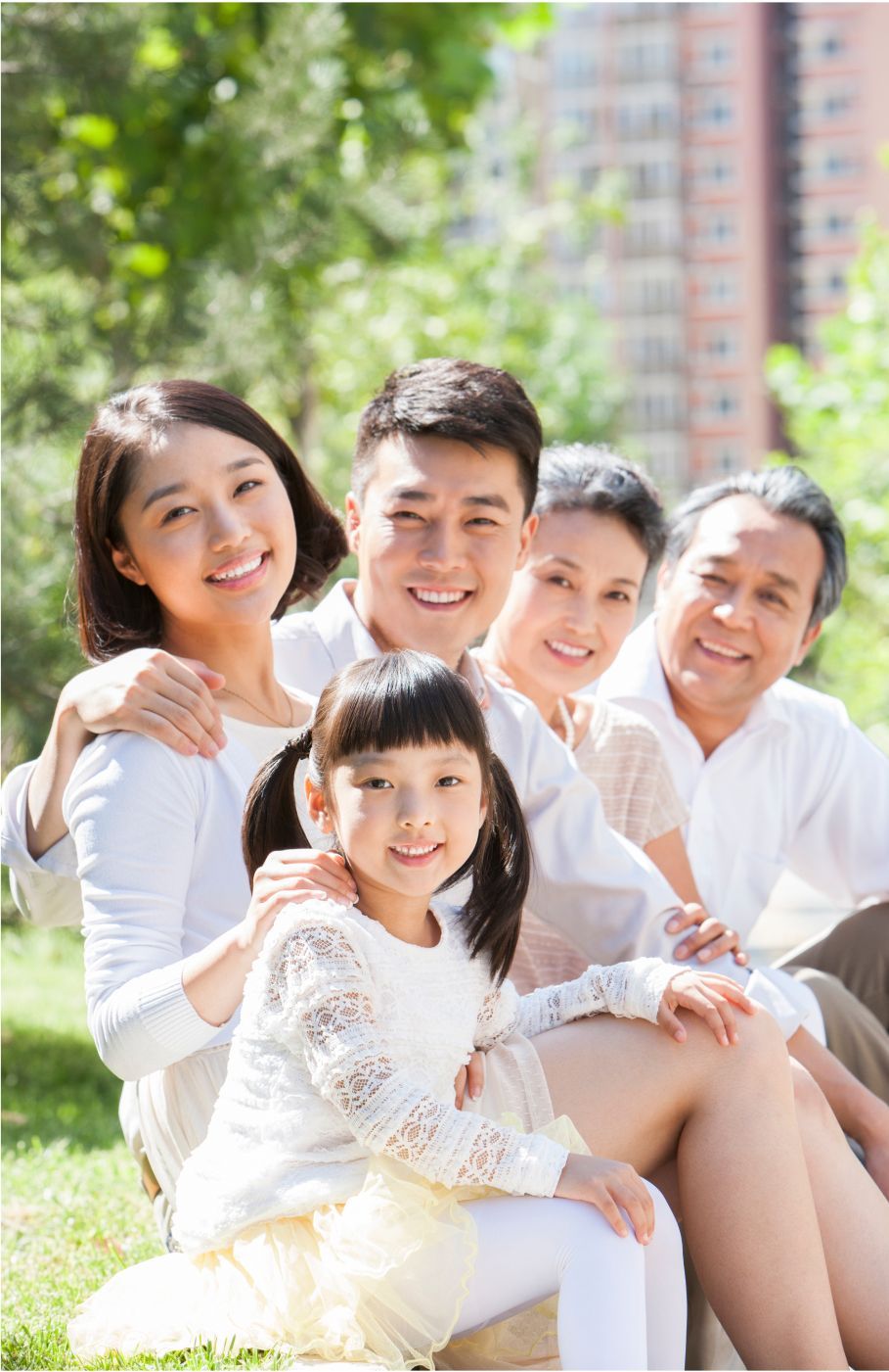 A family is posing for a picture while sitting on the grass in a park.