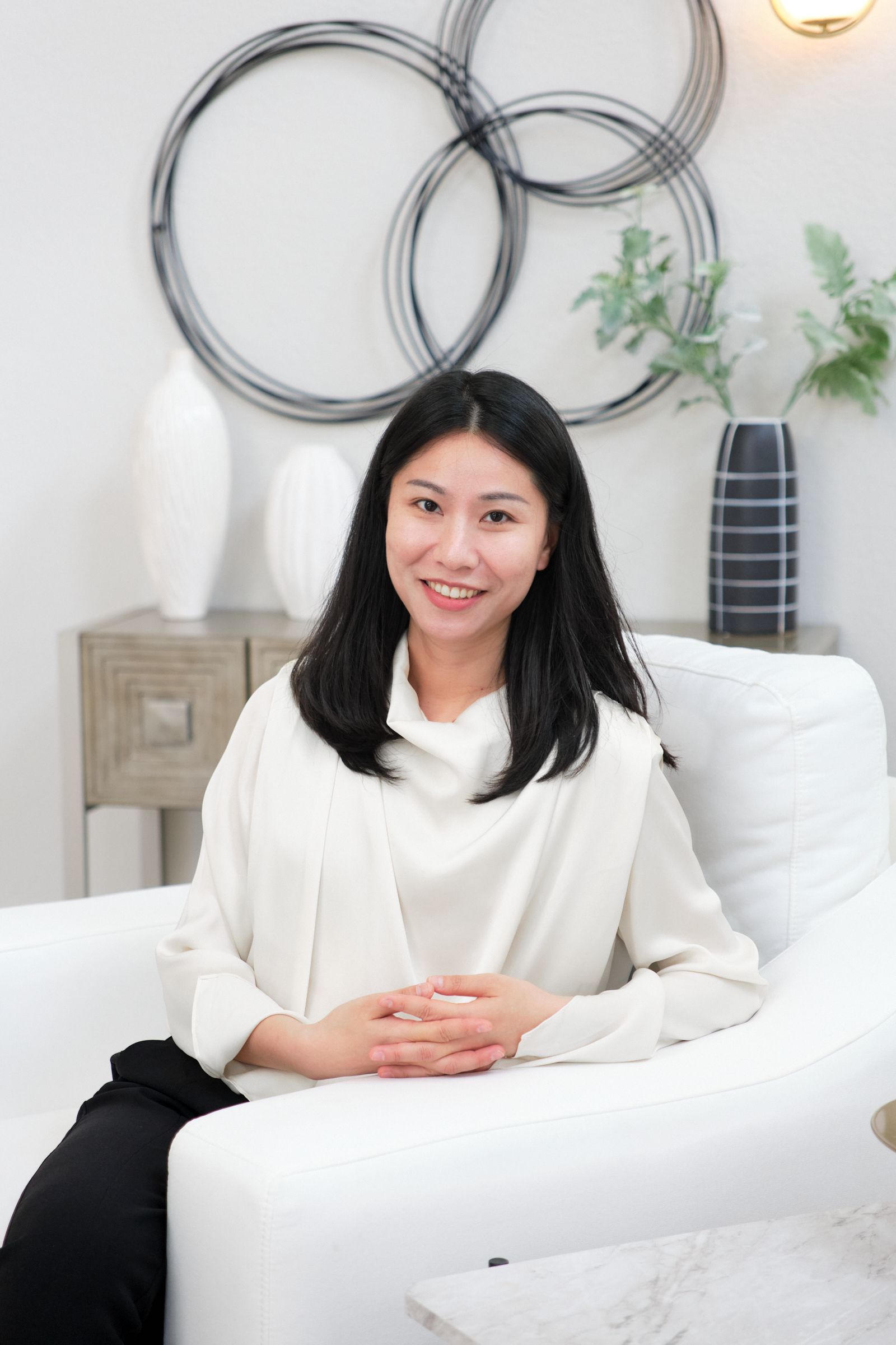 A woman is sitting on a white couch in a living room.