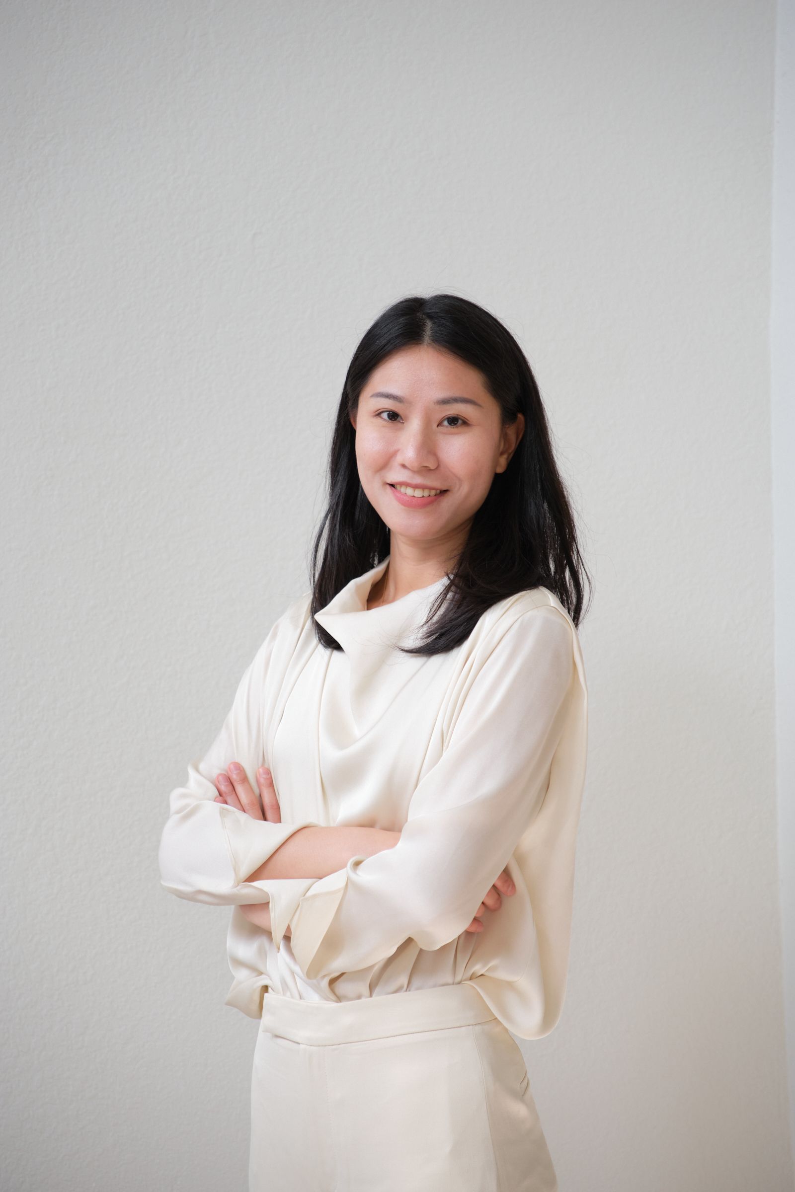 A woman in a white shirt and white pants is standing with her arms crossed.