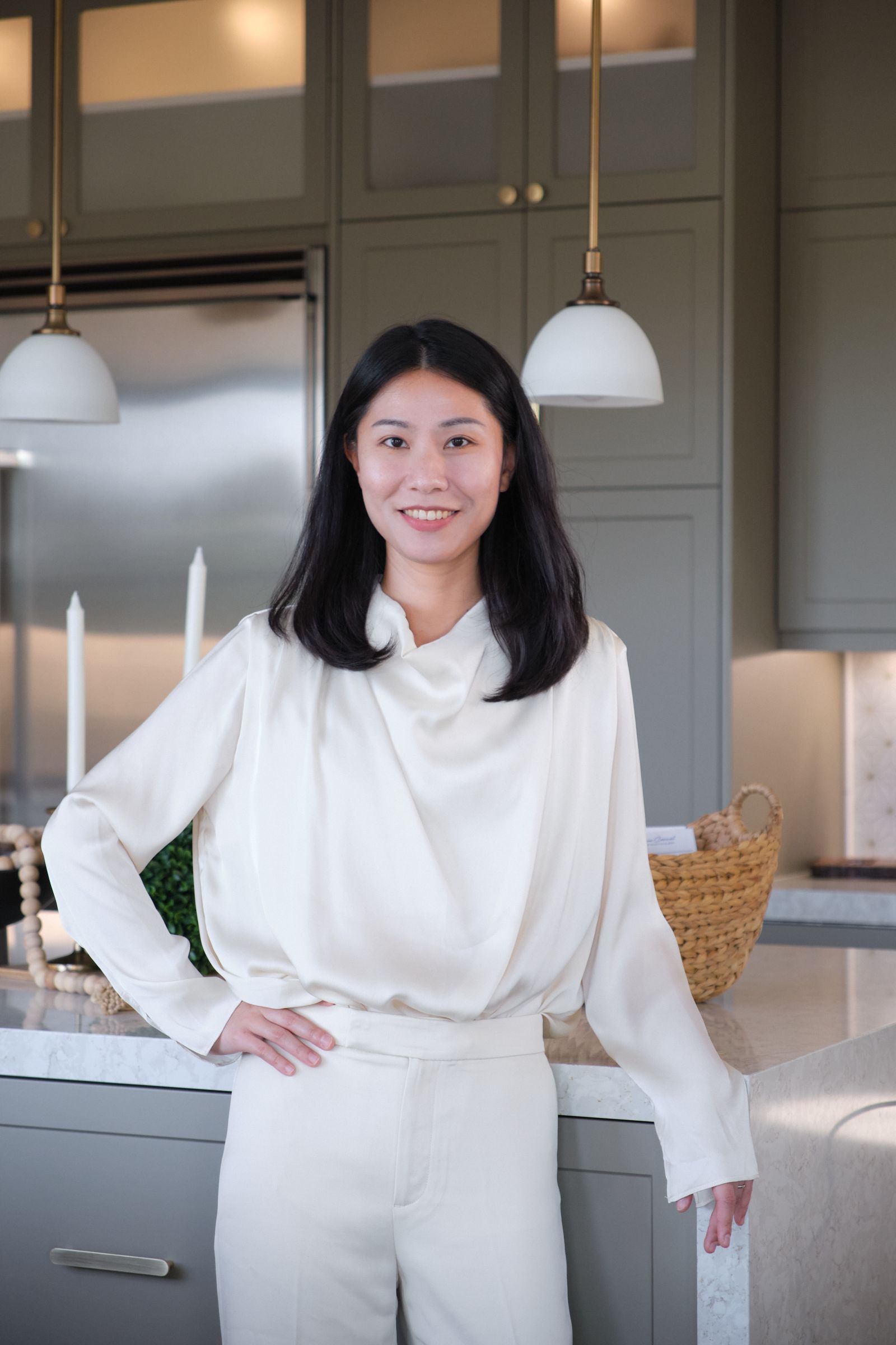 A woman in a white shirt and white pants is standing in a kitchen.