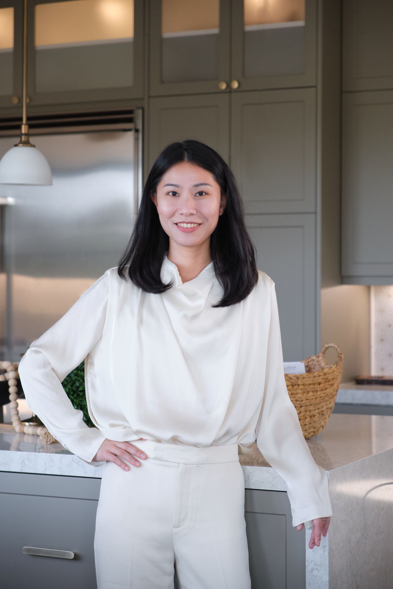 A woman in a white shirt and white pants is standing in a kitchen.