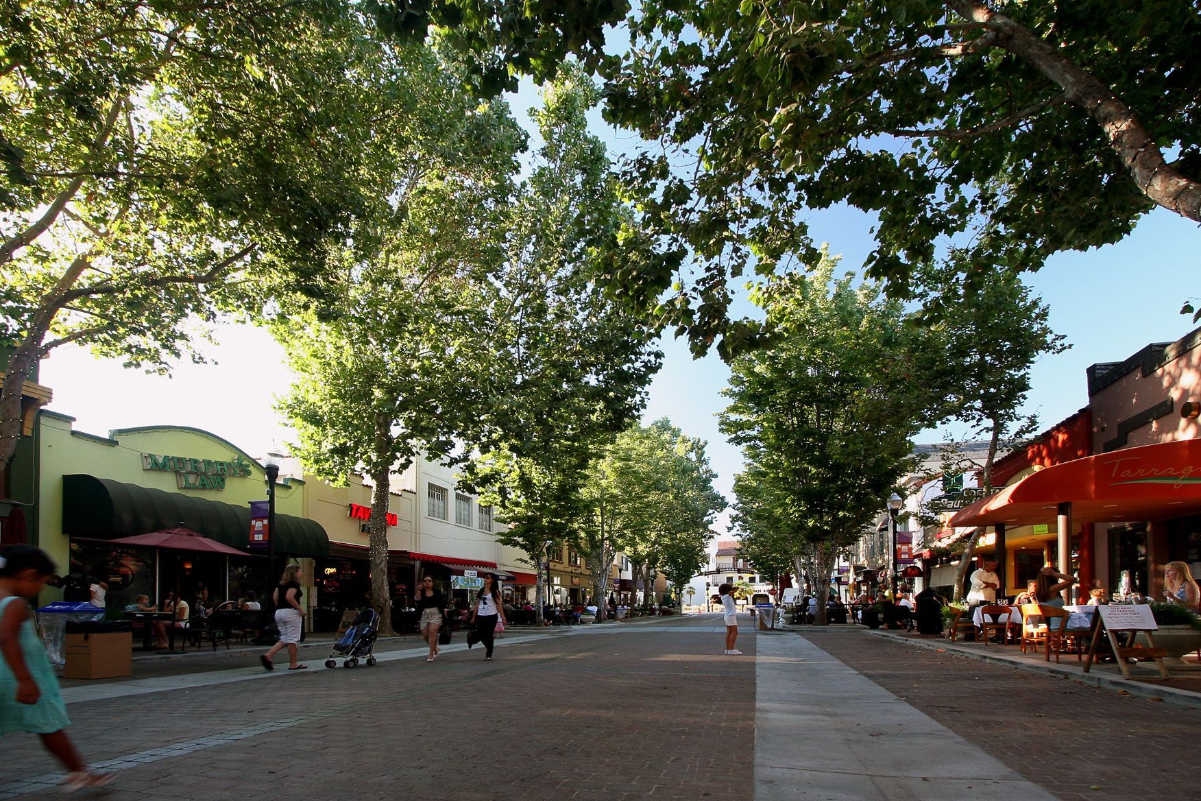People are walking down a street lined with shops and trees