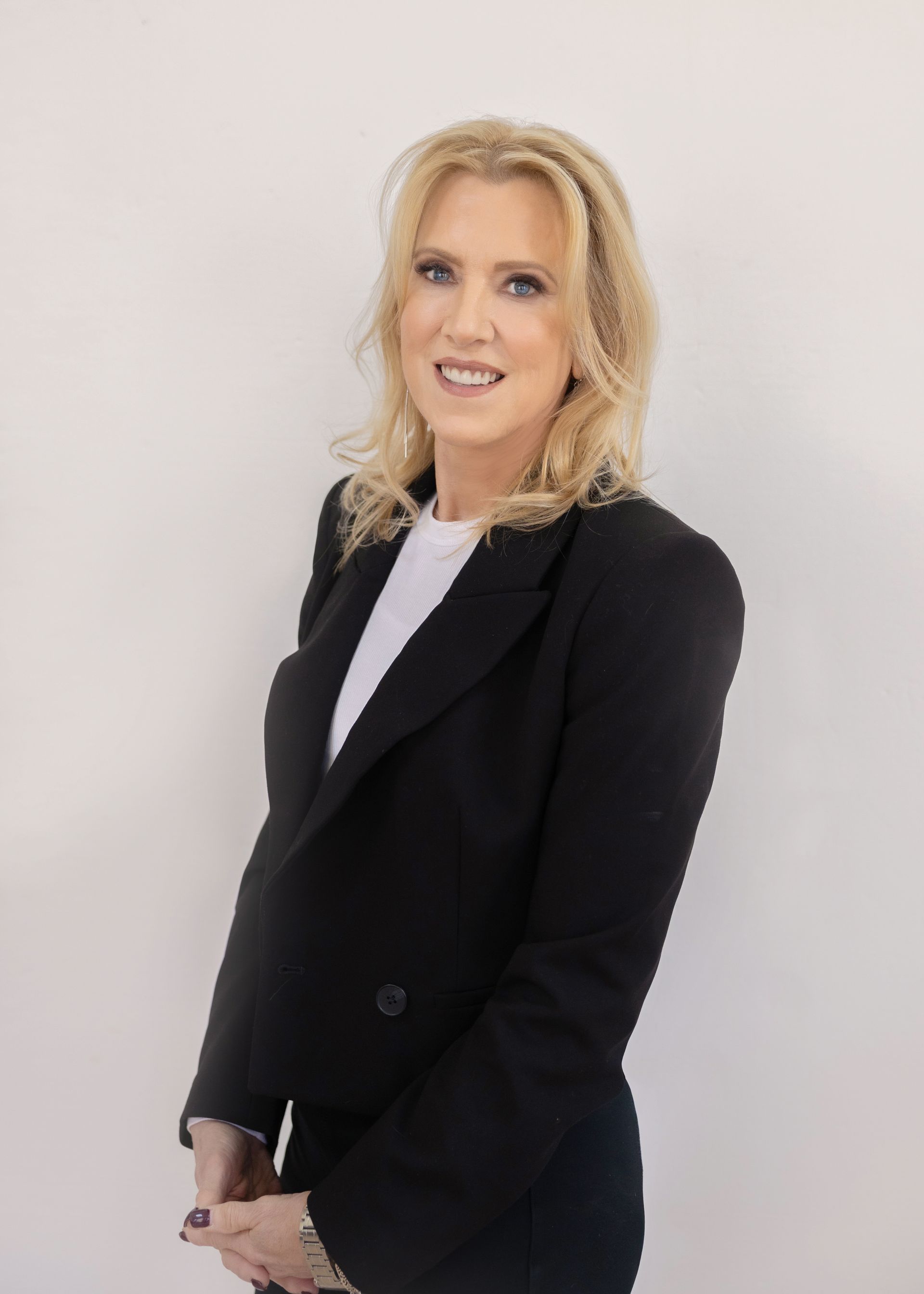 A woman in a black jacket and white shirt is standing in front of a white wall.