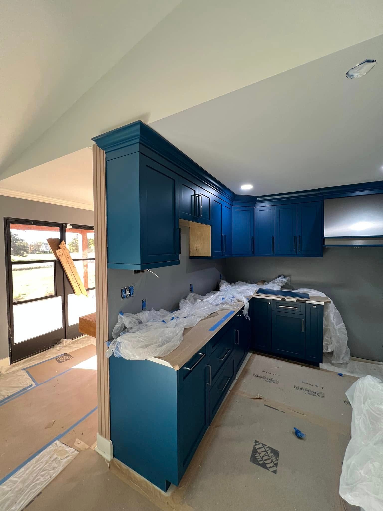 A partially constructed kitchen with dark blue cabinets. The room is under construction.