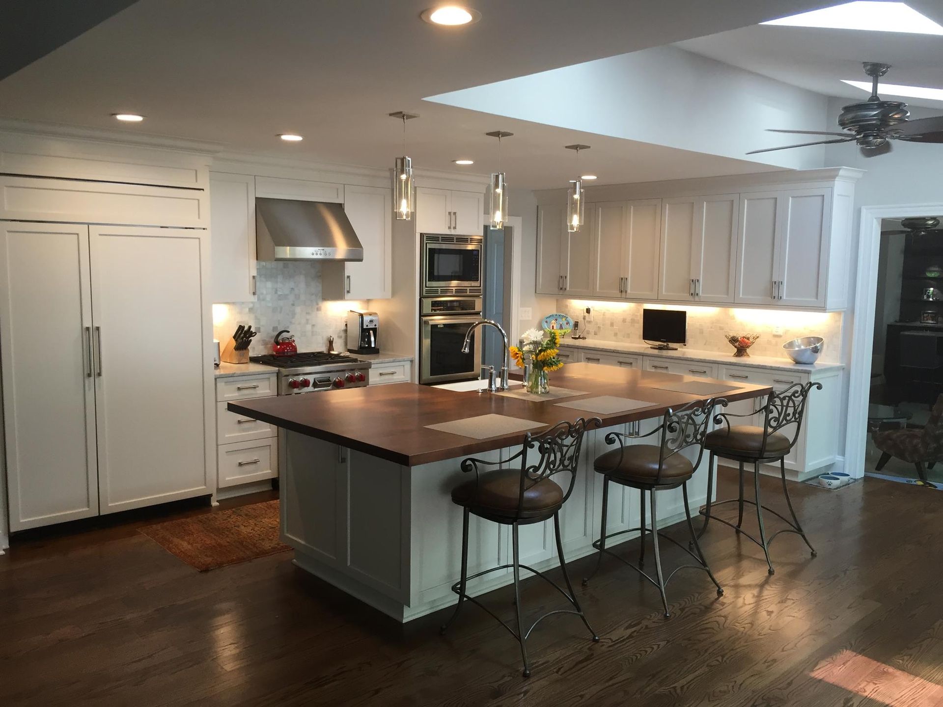 A white kitchen with a large island, stainless steel appliances, and a skylight.