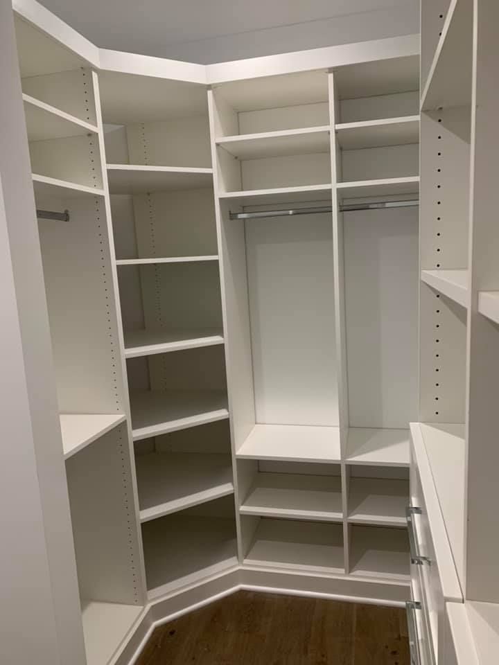 White built-in closet with shelves, a hanging rod, and drawers; the space is empty with a wood floor.