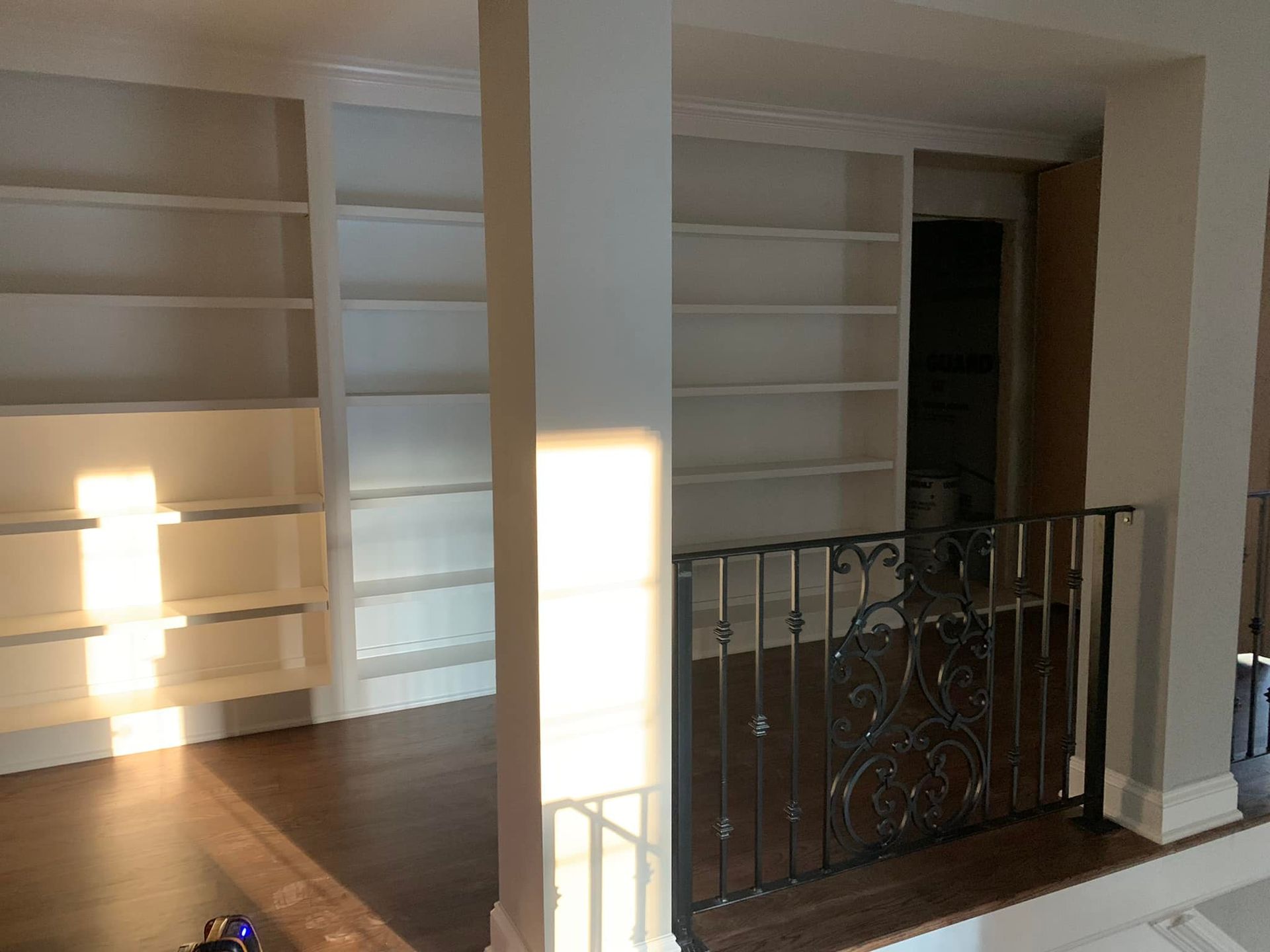 Built-in white bookshelves on a landing above a dark wood floor and a black wrought iron railing.