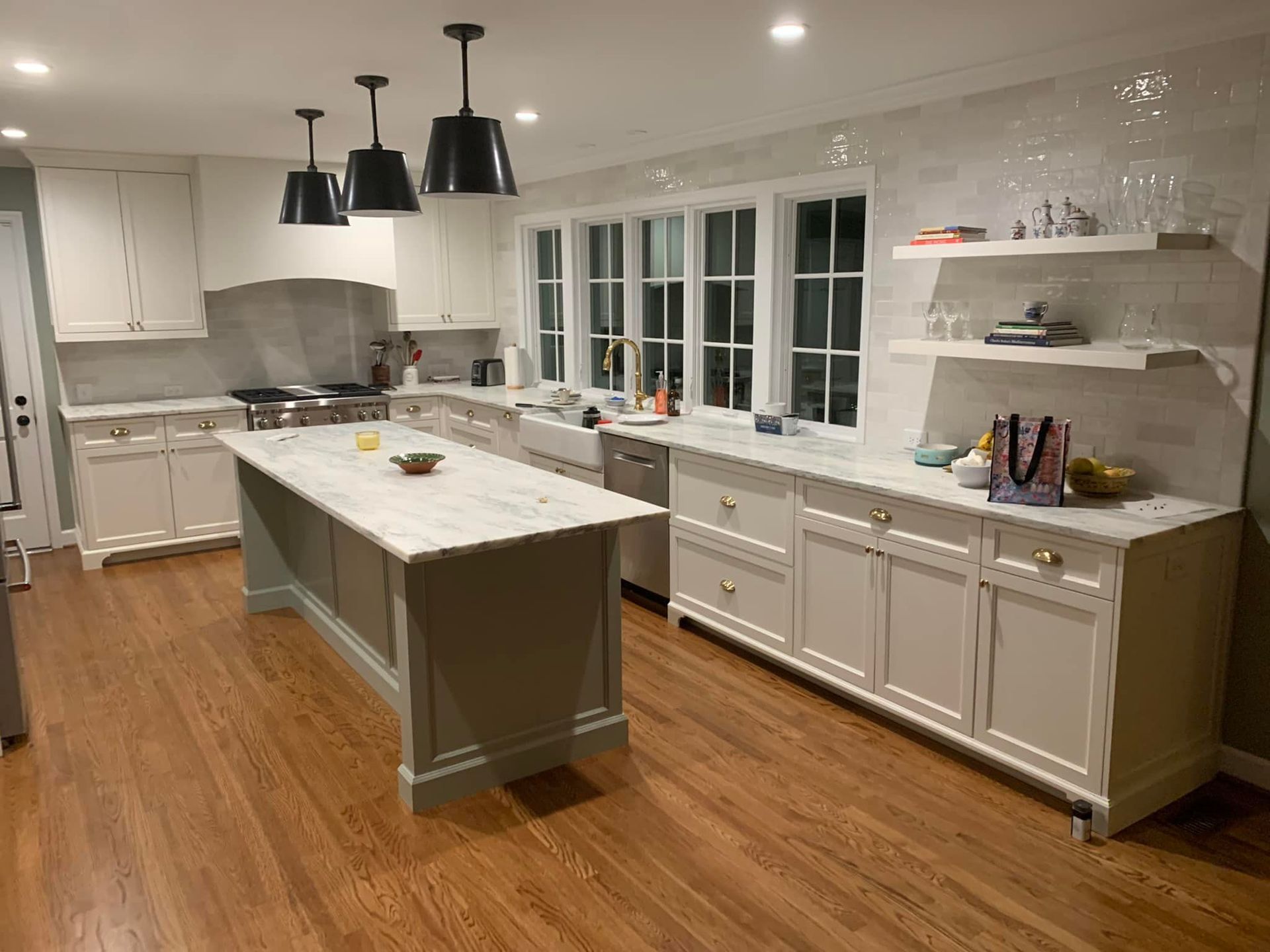 Spacious, bright kitchen with white cabinetry, a large island, and wood flooring. Overhead, three black pendant lights hang.