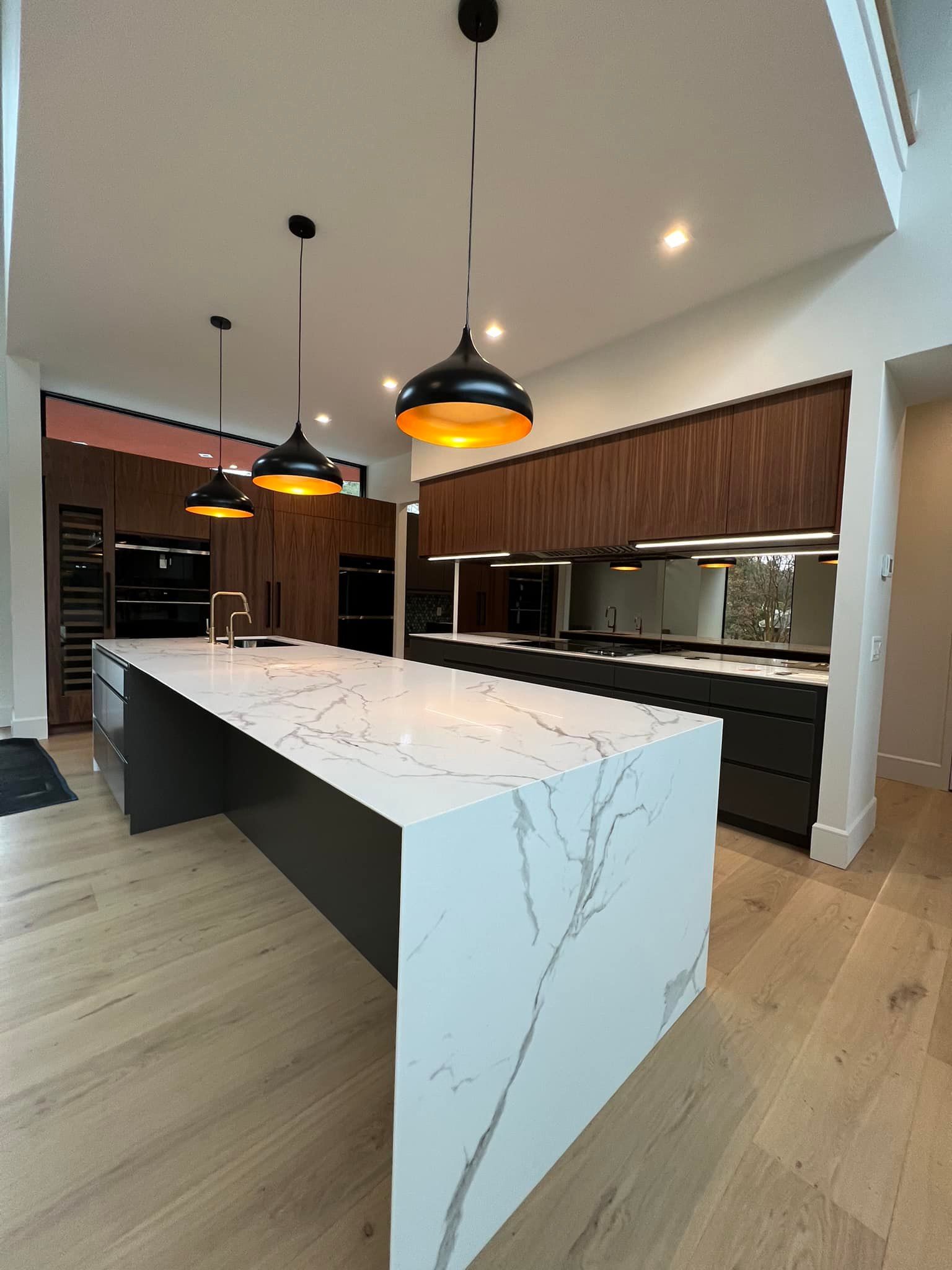 Modern kitchen with a large marble island, dark cabinets, and black pendant lights.