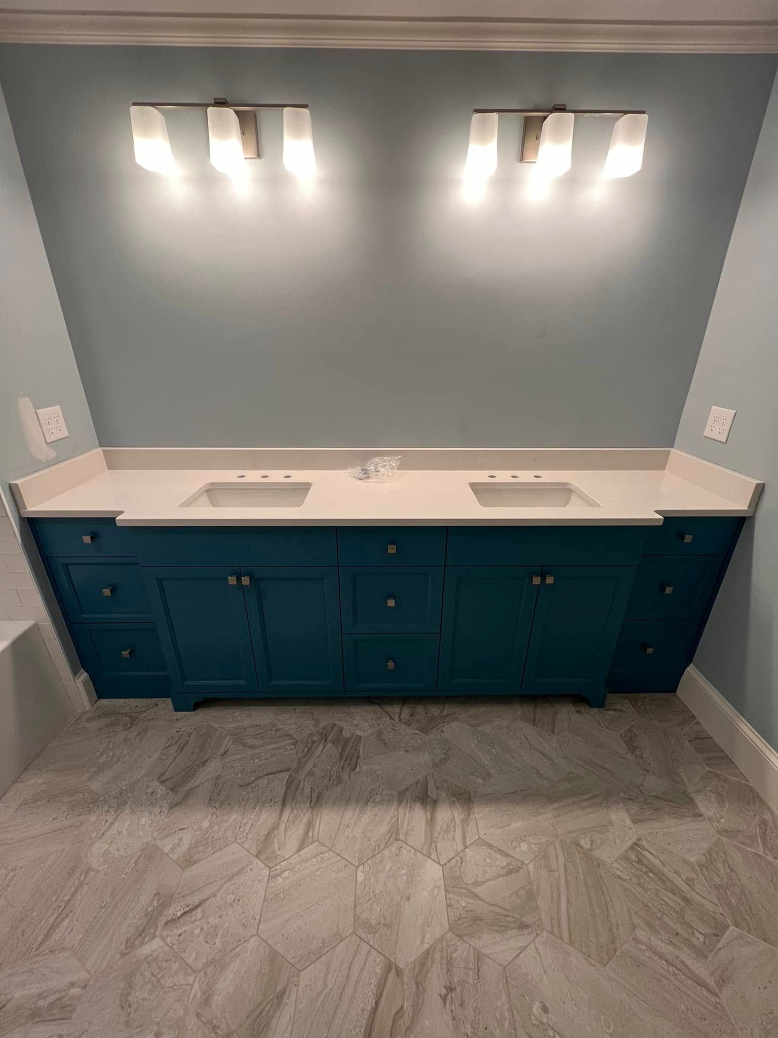 Teal double vanity with white countertop and sconce lighting against a blue wall. Gray tile flooring.