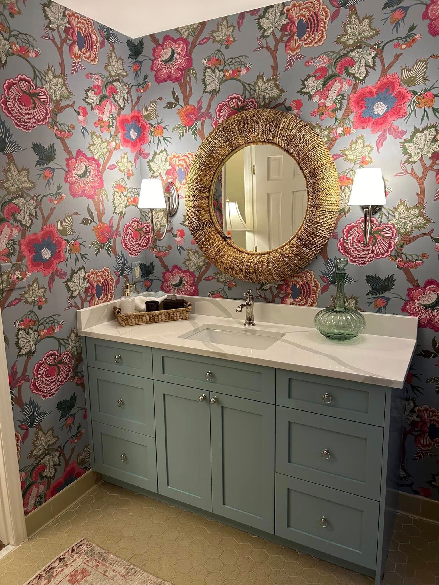 Powder room with floral wallpaper, light blue vanity, gold mirror, and sconces.