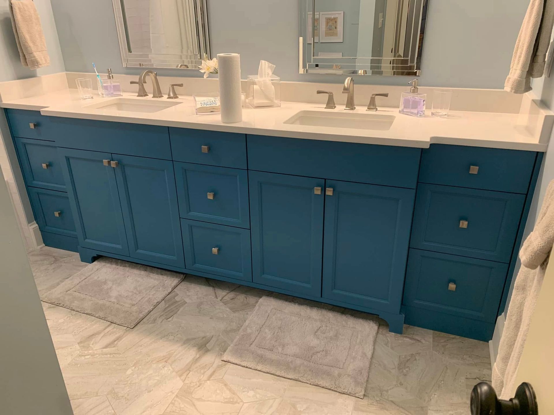 Blue double vanity bathroom with white countertop and two sinks, two mirrors, and gray rugs.