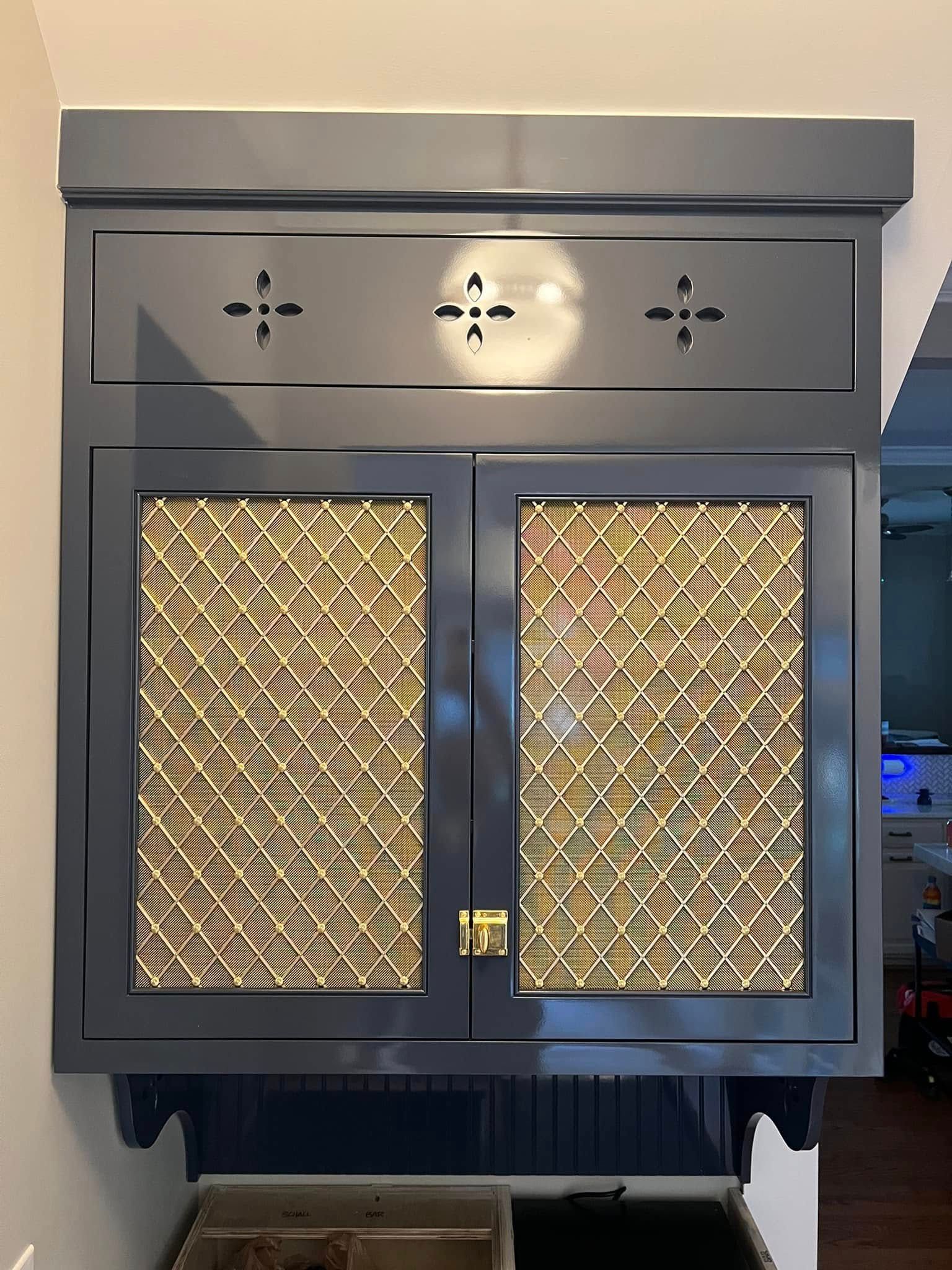 Dark blue kitchen cabinet with diamond-patterned door inserts. It is mounted on a wall with a decorative top and bottom trim.