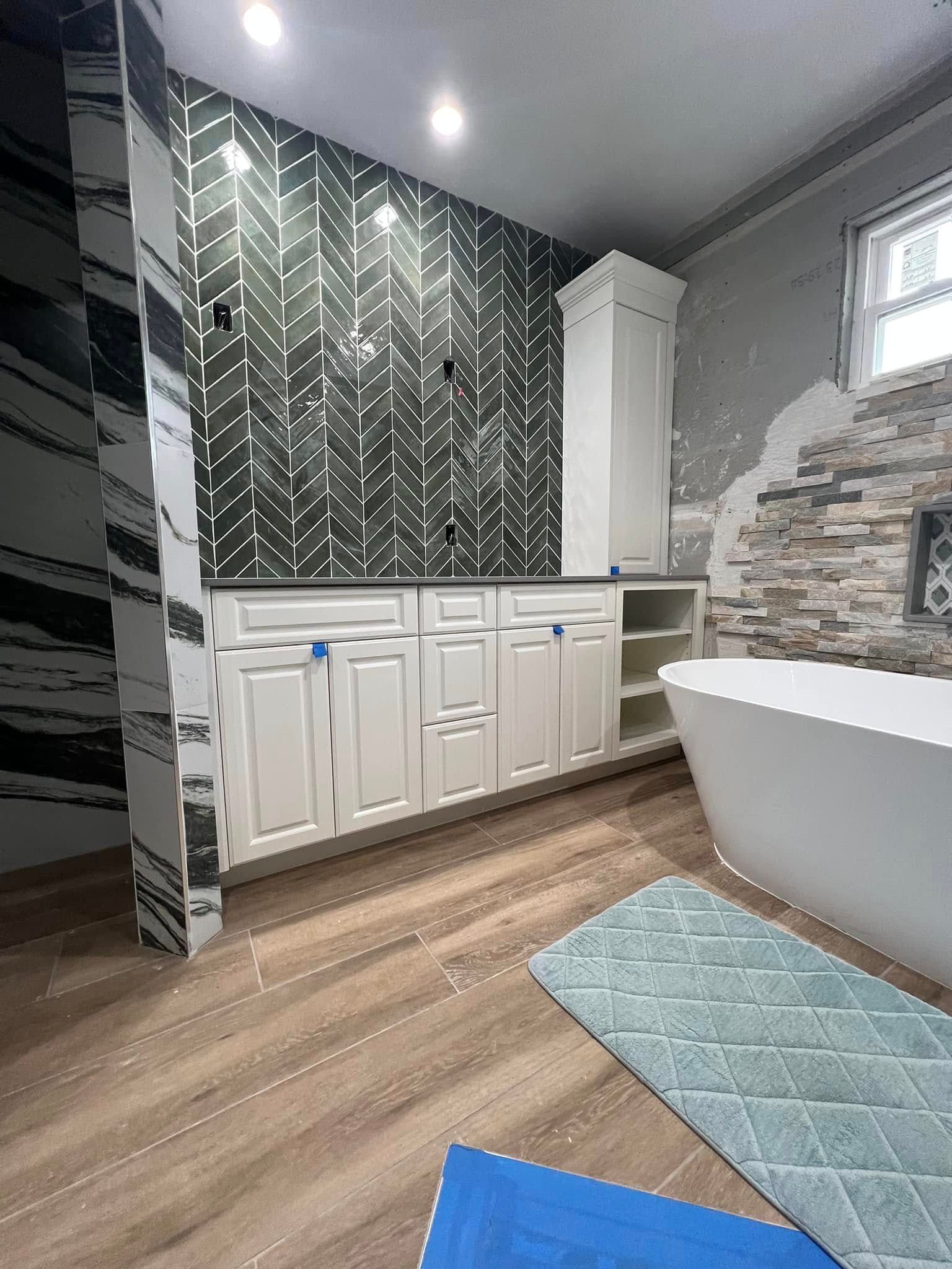 Bathroom under construction featuring white cabinets, patterned black and white tile, and a freestanding tub.