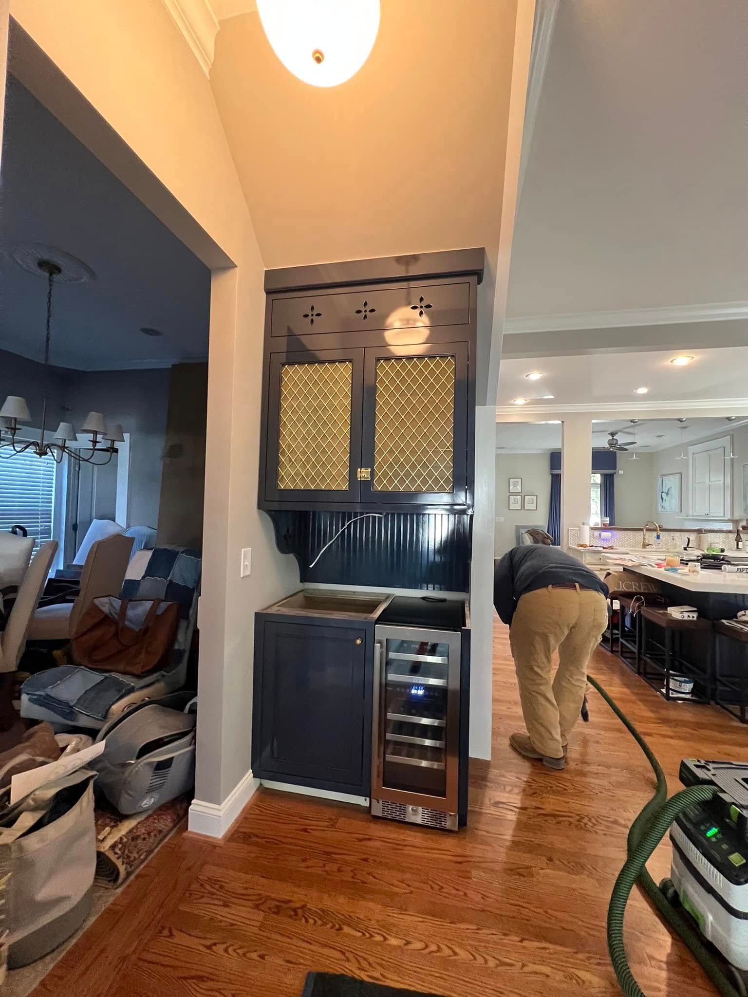 A person working on a dark grey bar cabinet with a wine fridge.