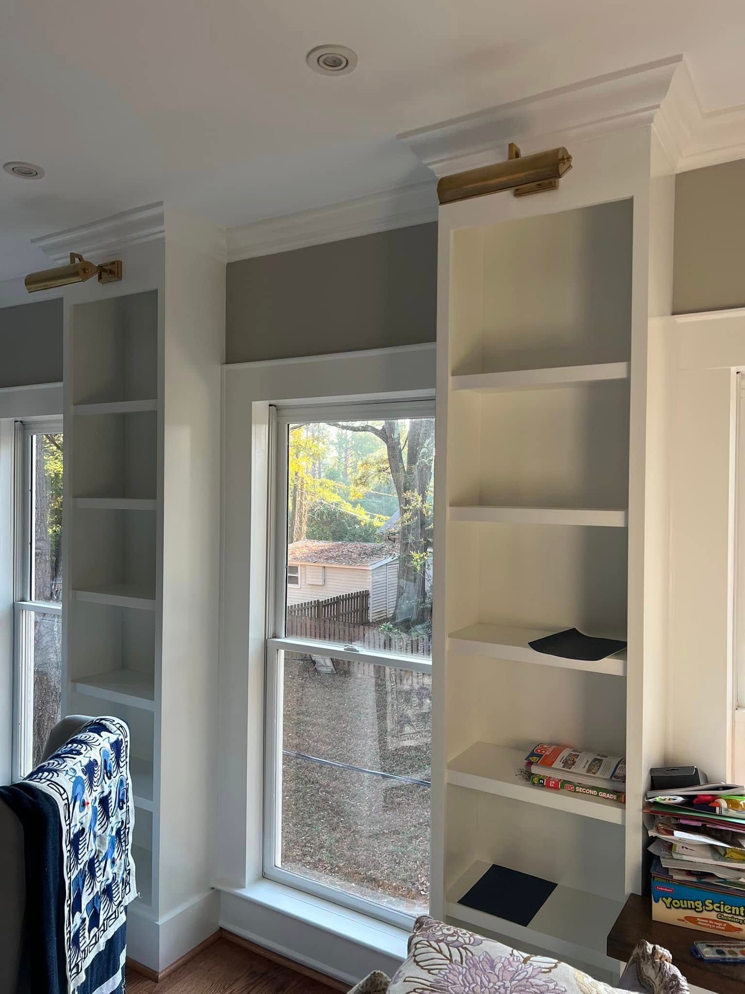 Two white bookshelves flanking a window. Gold light fixtures are mounted above the shelves.