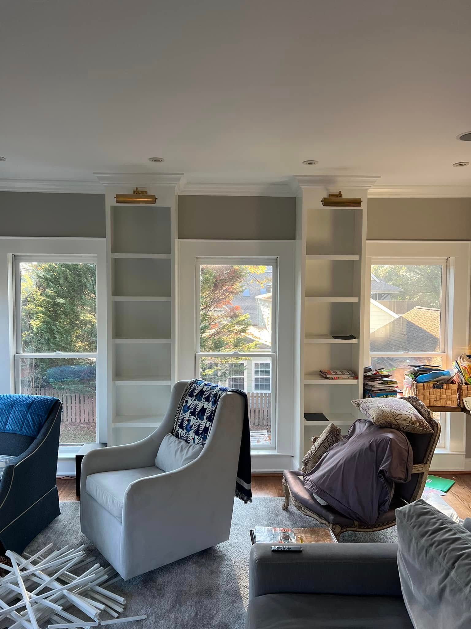 Living room with white bookshelves flanking windows. A gray chair and a blue couch are visible, along with a patterned rug.