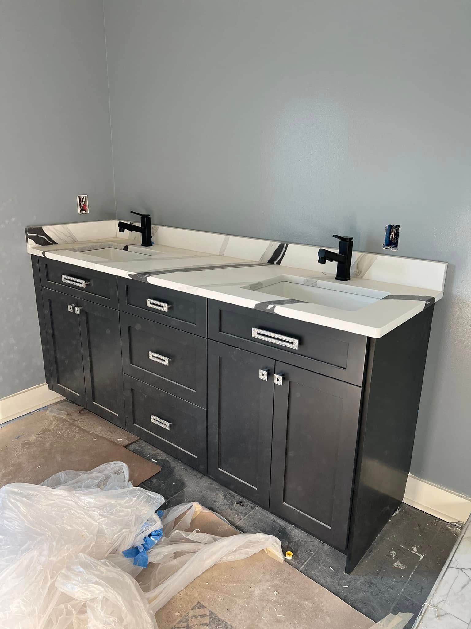 A dark gray double vanity with white countertops and black faucets installed in a bathroom with gray walls.