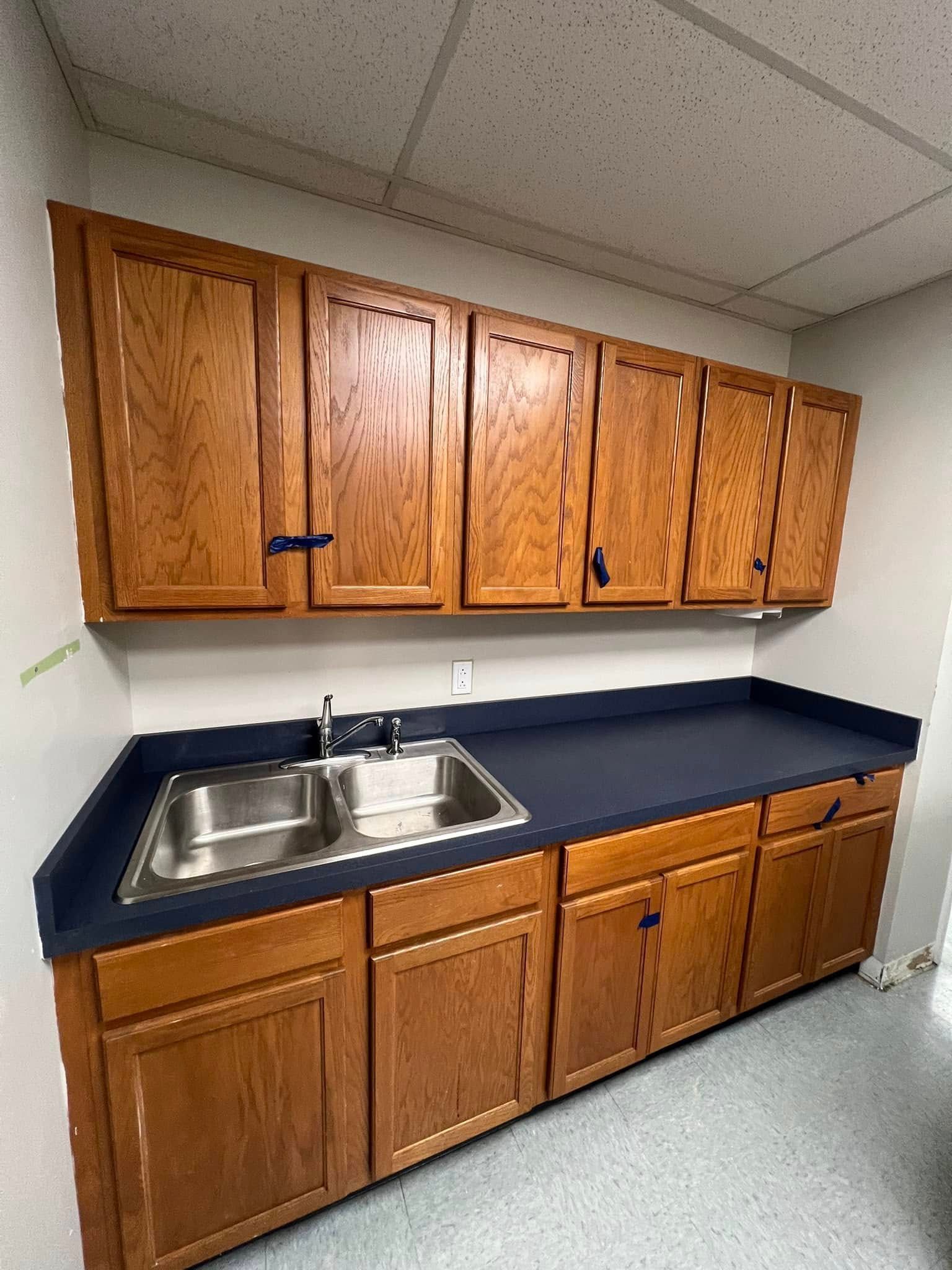 Wooden cabinets, a sink, and a dark countertop against a wall.