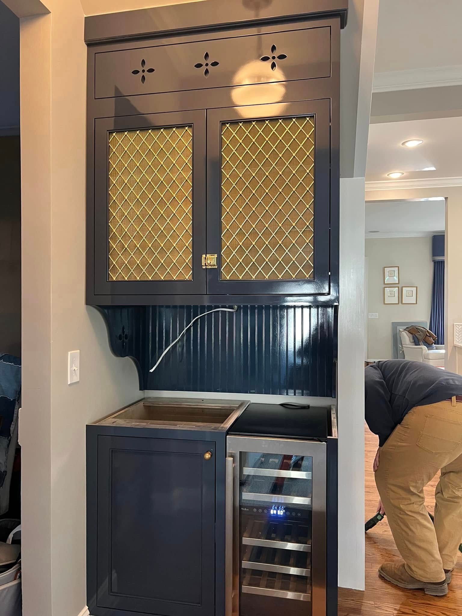 Navy blue wet bar with gold lattice cabinet doors and wine fridge; a person is visible to the right.