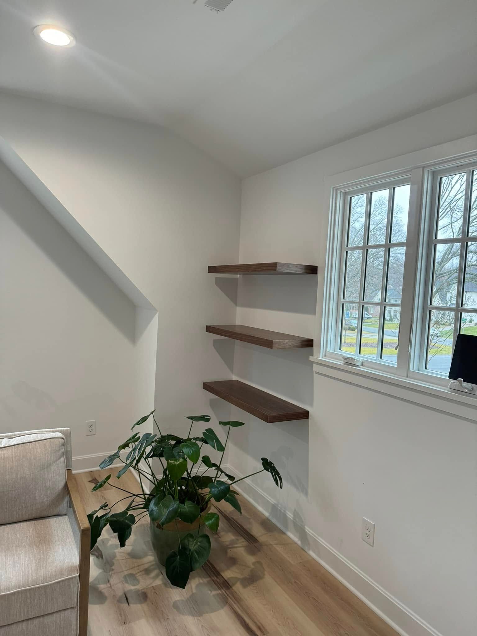 A room with built-in shelves and a window, featuring a plant in a pot and a neutral-toned couch.