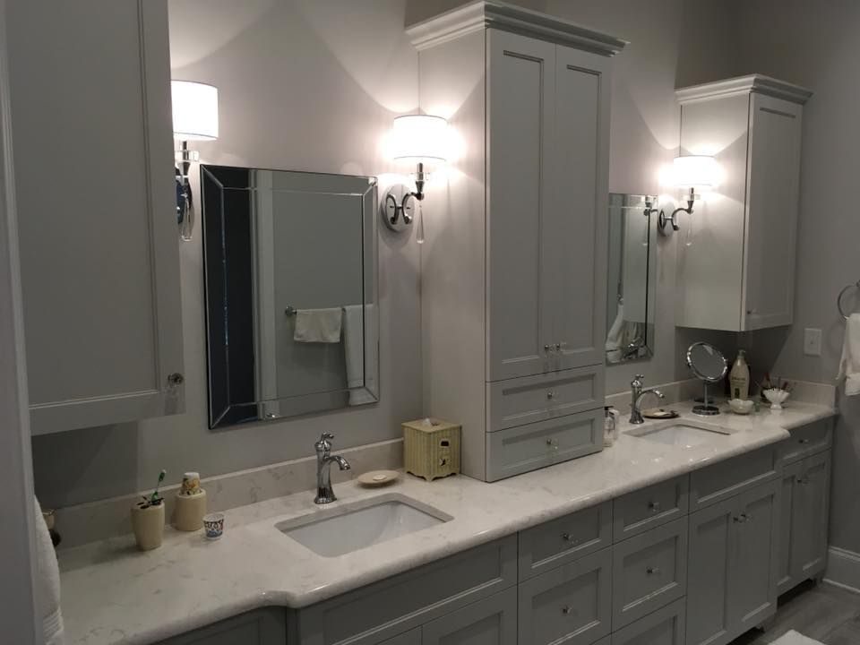 A modern bathroom with gray cabinets, white countertops, and bright sconce lighting.