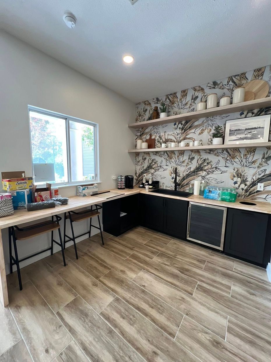 A well-lit craft room with a long desk, black cabinets, shelves with decor, and a floral wallpaper accent wall.