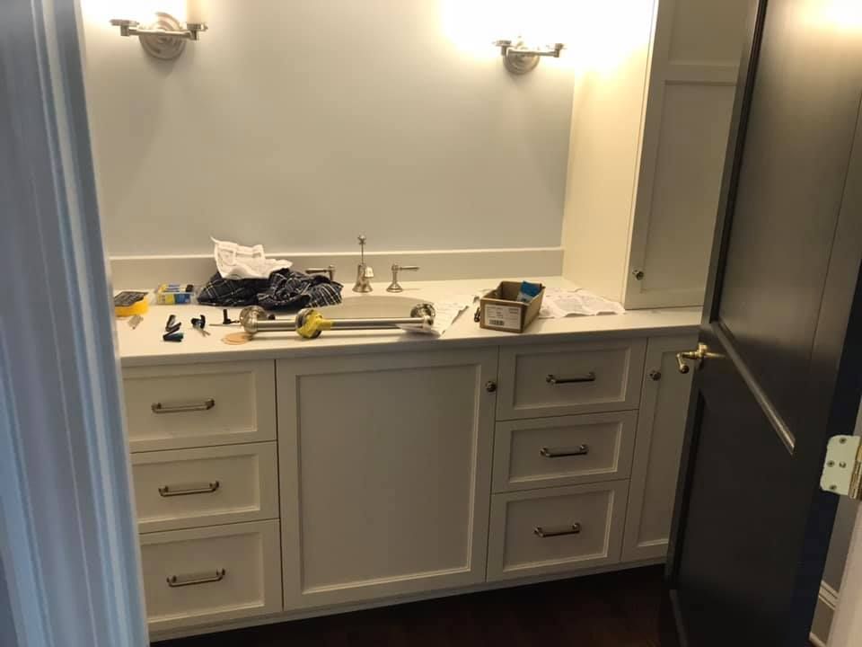 Bathroom with white vanity, countertop, and cabinets; tools and supplies on the counter. Two sconce lights above.