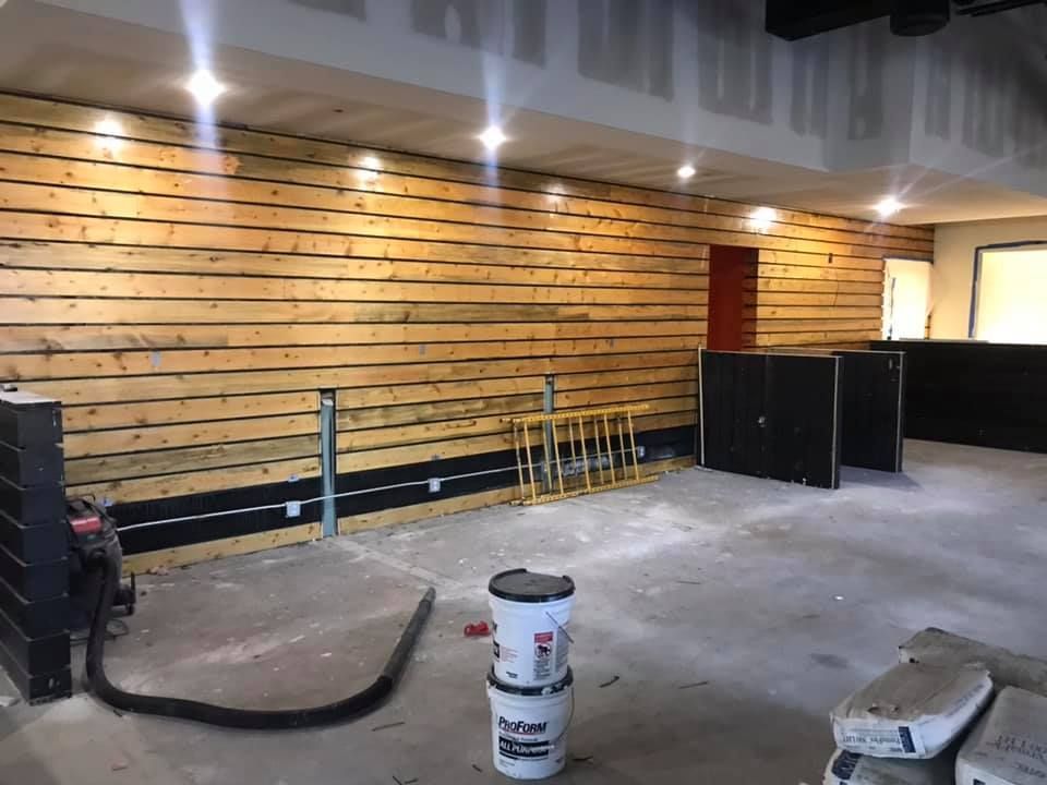 A room under construction. Wooden paneling on the wall, concrete floor, and construction materials visible.