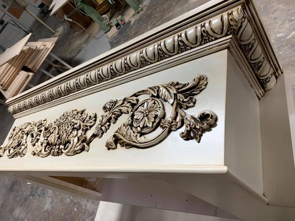 Cream-colored, ornate wooden cabinet with decorative carvings, likely part of a larger piece of furniture.