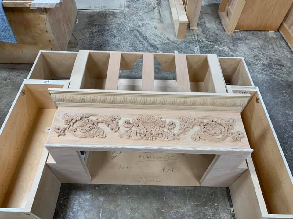 Wooden fireplace mantel under construction, featuring detailed carved ornamentation