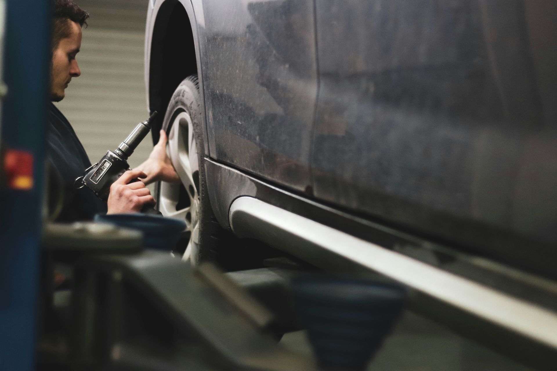 Mechanic removing a tire from a car on a lift in a garage.