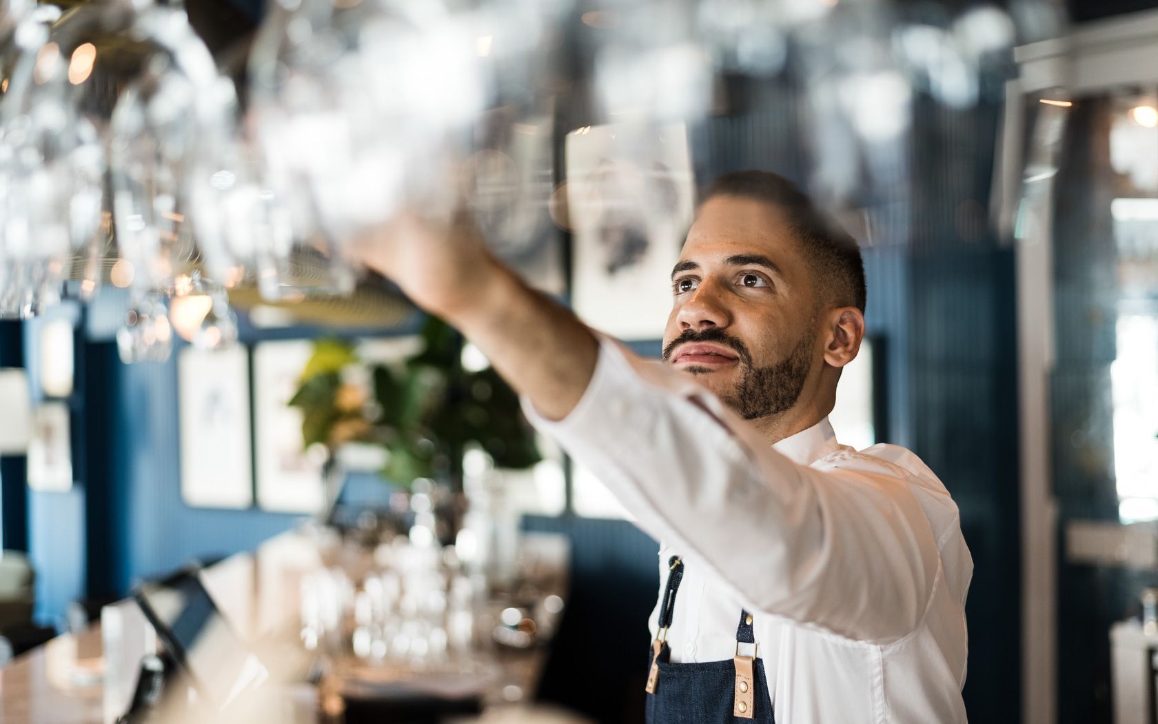 Bartender reaching for a glass hanging overhead