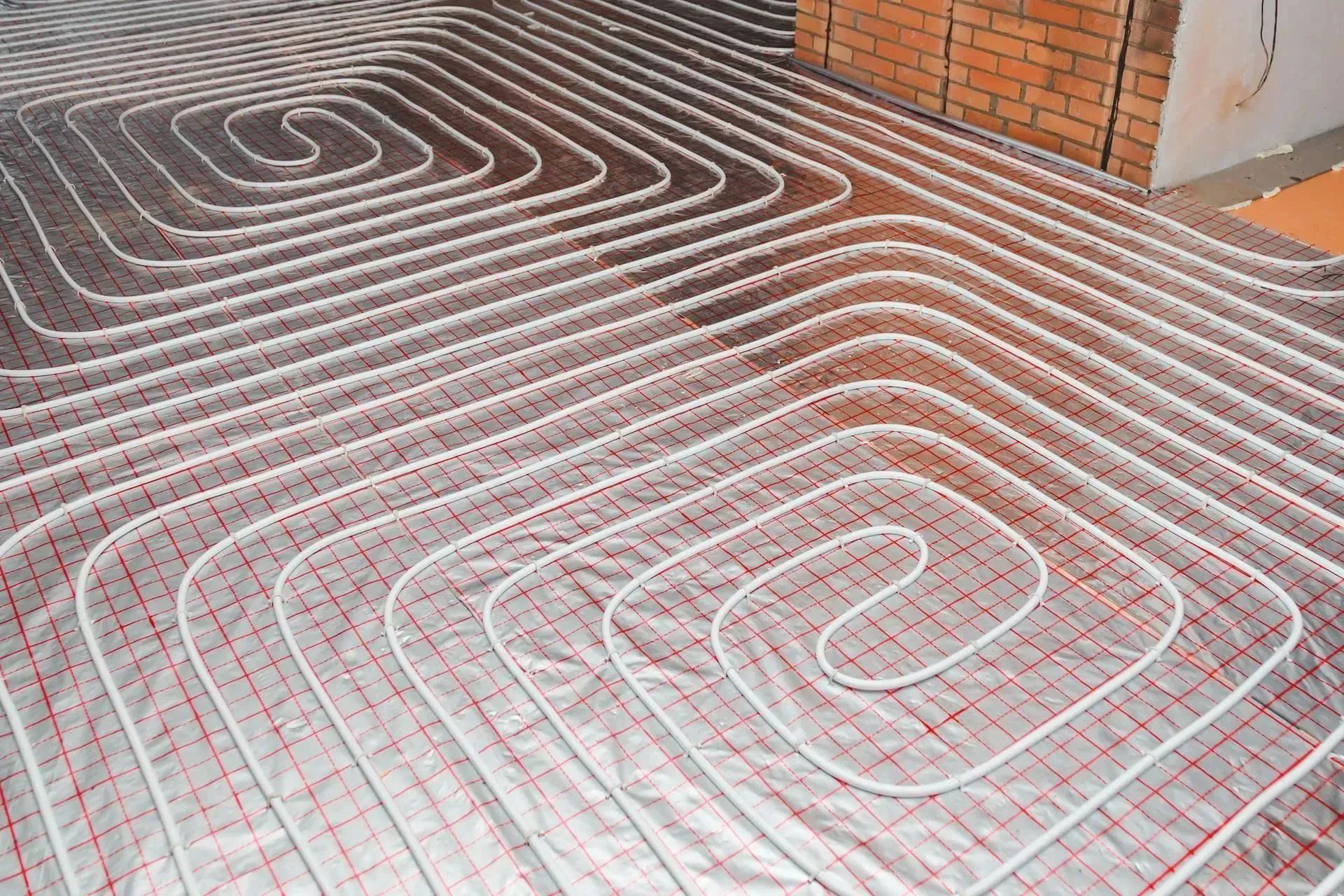 Underfloor heating system with coiled pipes on a grid surface, near a brick wall.