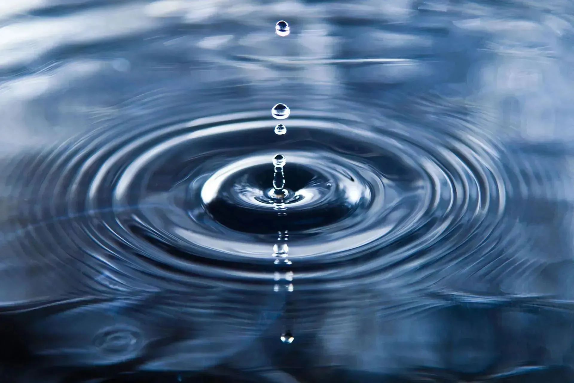 A close-up of water droplets creating ripples on a calm surface.