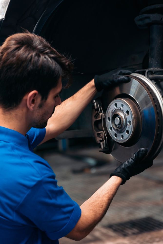 A Man In A Blue Shirt Is Fixing A Brake Disc On A Car — Transtate Trailers & 4wd In Belconnen, ACT