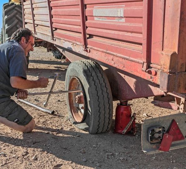 A man is kneeling down to change a tire on a trailer — Transtate Trailers & 4wd In Belconnen, ACT