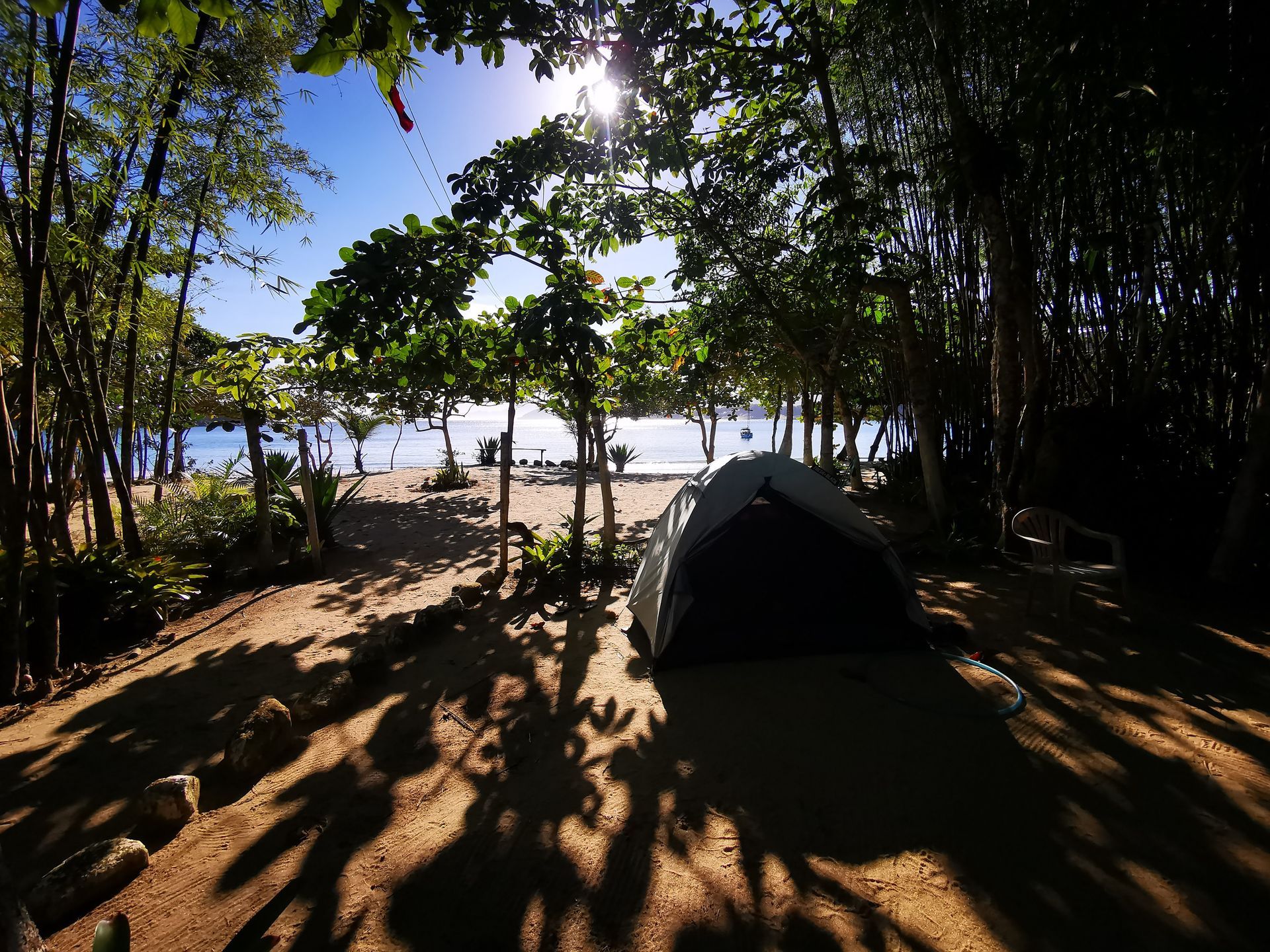 Área de camping tranquila em Parnaioca, Ilha Grande, com uma barraca montada sob a sombra de árvores tropicais, de frente para uma praia de areia e águas calmas ao fundo, criando um ambiente sereno e natural, perfeito para entusiastas de atividades ao ar livre