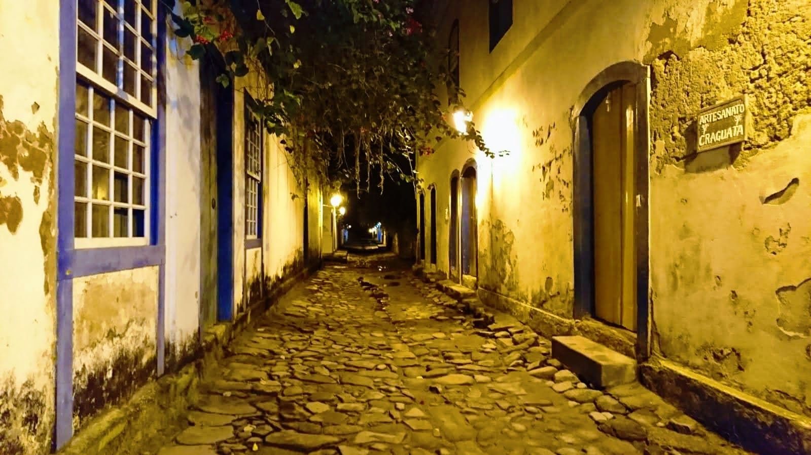 Alt text: Narrow cobblestone street in Paraty, Rio de Janeiro, at night, with colonial-style buildings, warm street lighting, and overhanging vines.