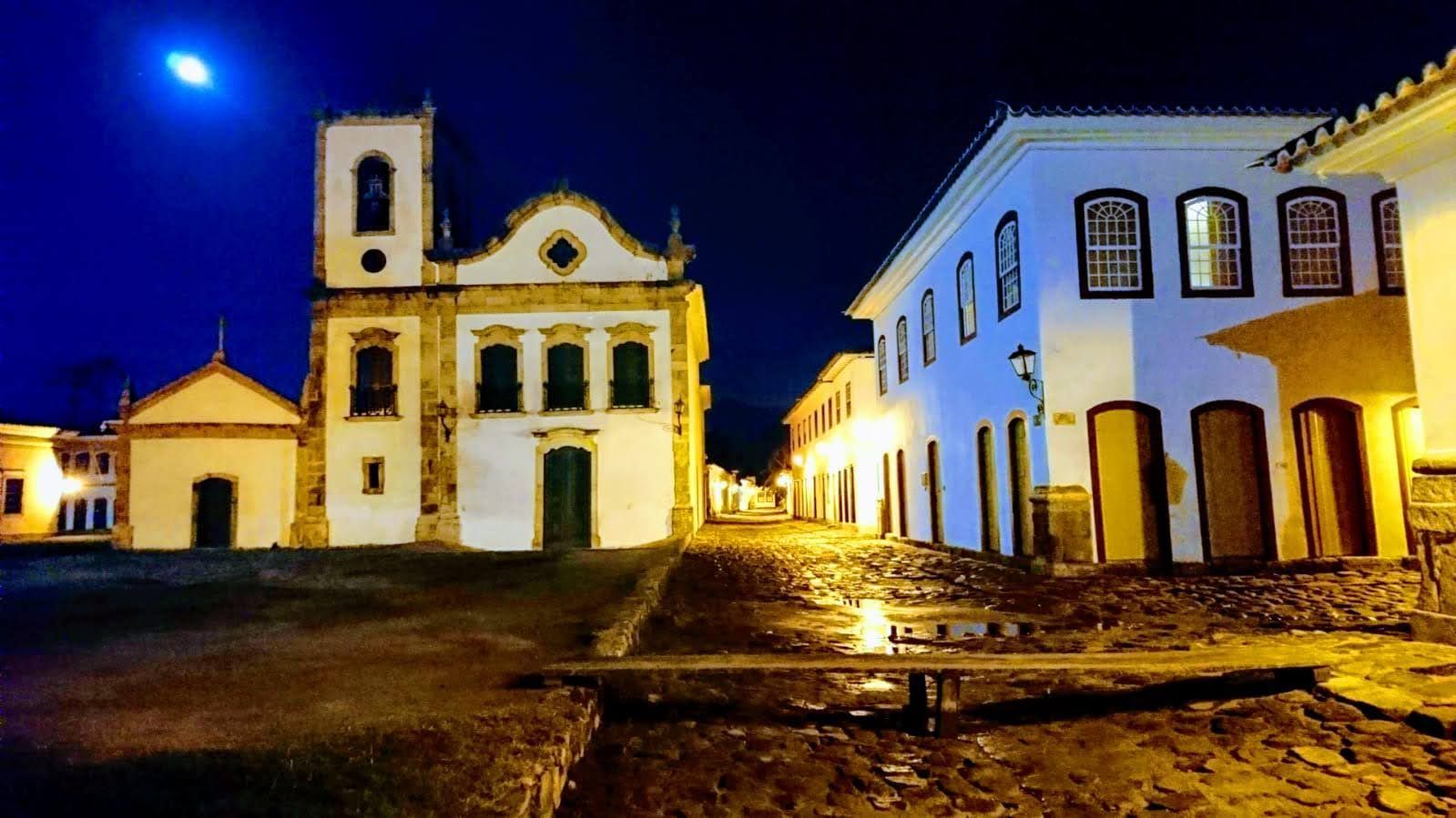 This image appears to depict a nighttime scene in a colonial town square, featuring historic buildin